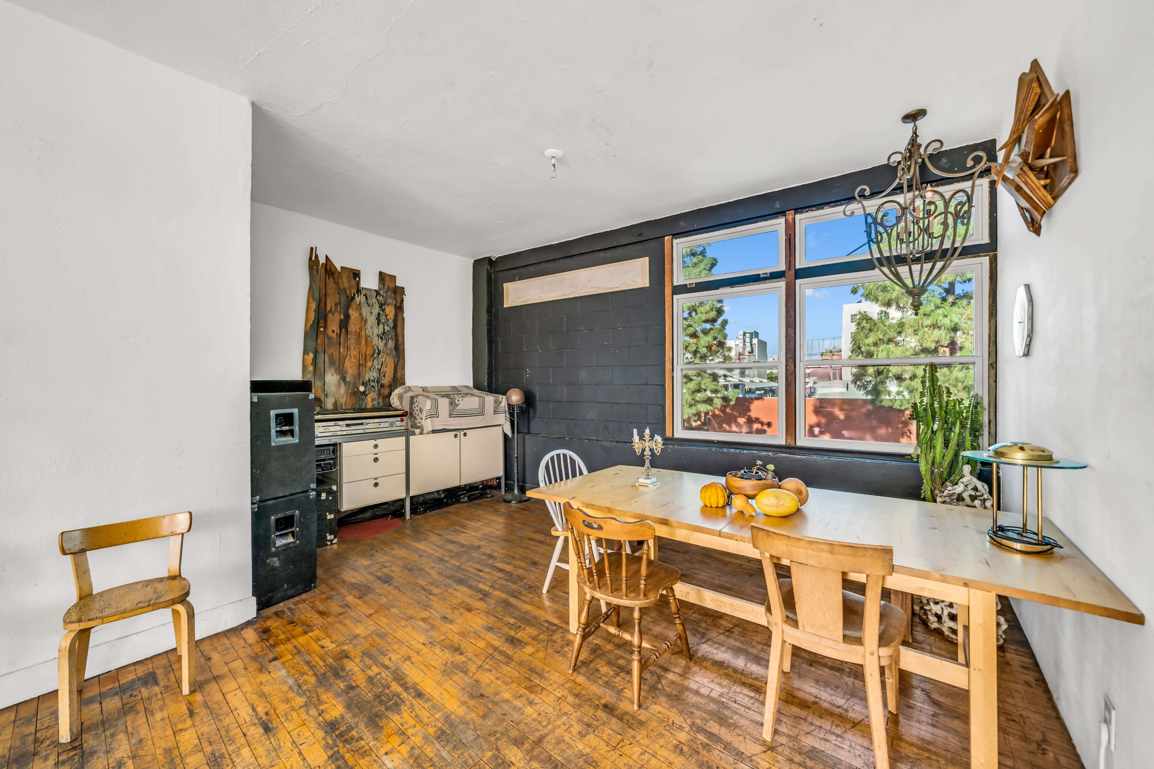 The image shows a dining area with a wooden table and chairs, a vintage sideboard, and large windows allowing natural light to enter.