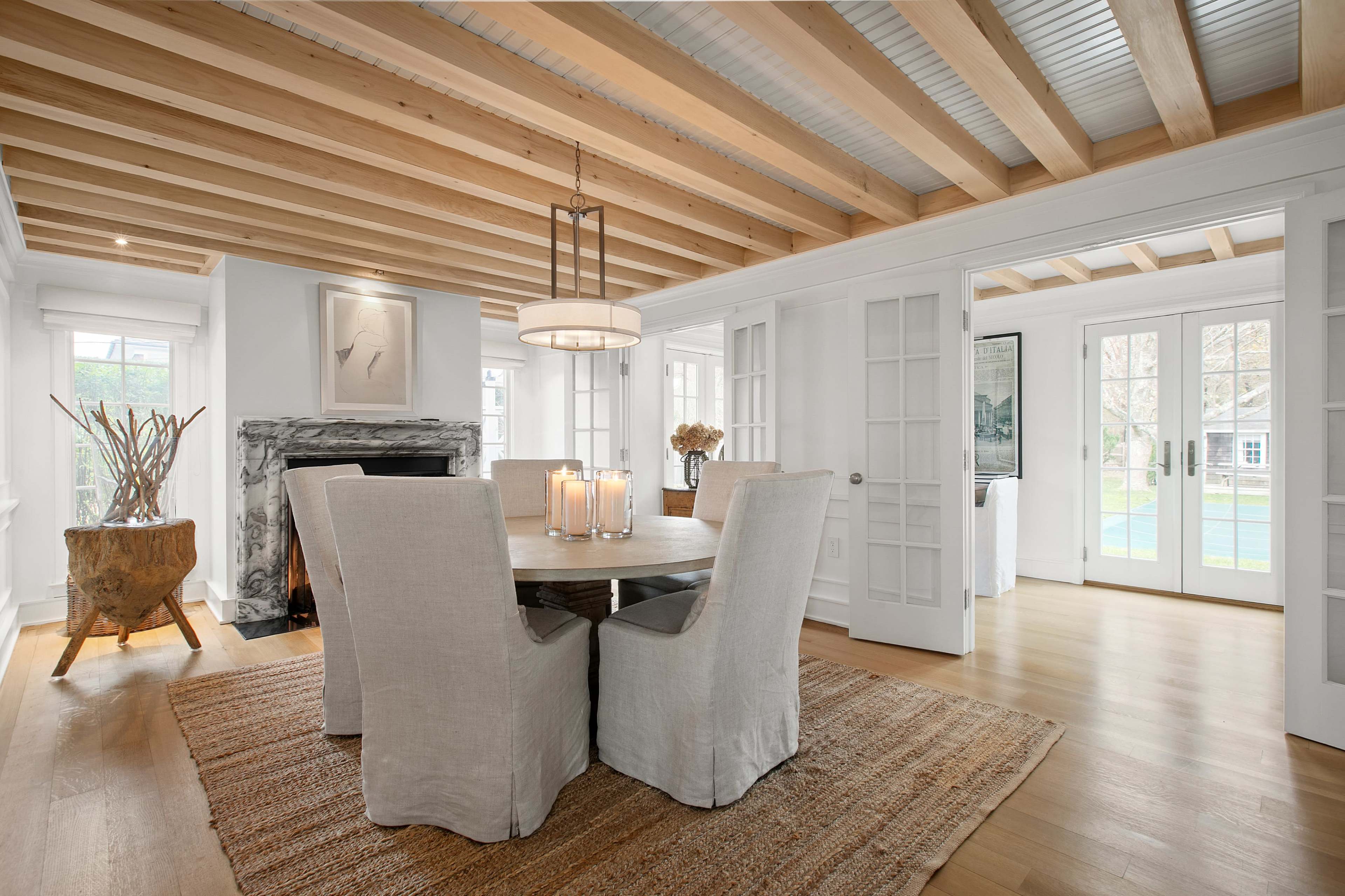 A dining area features a wooden table surrounded by upholstered chairs, a decorative rug, and a stone fireplace, with large glass doors leading to an outdoor space.