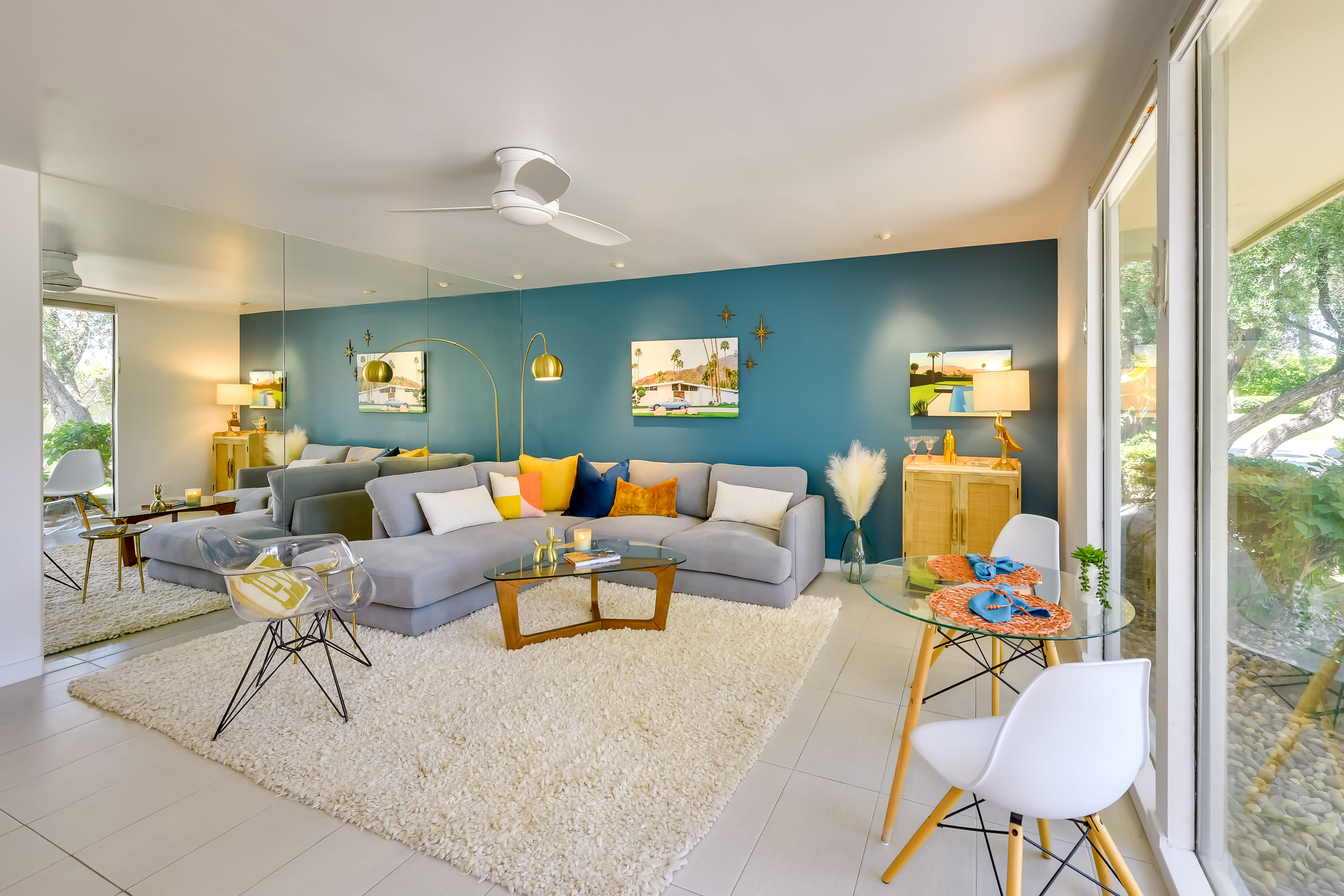 The image shows a modern living room featuring a sectional sofa, decorative pillows, a large area rug, and a mirrored wall with artwork.