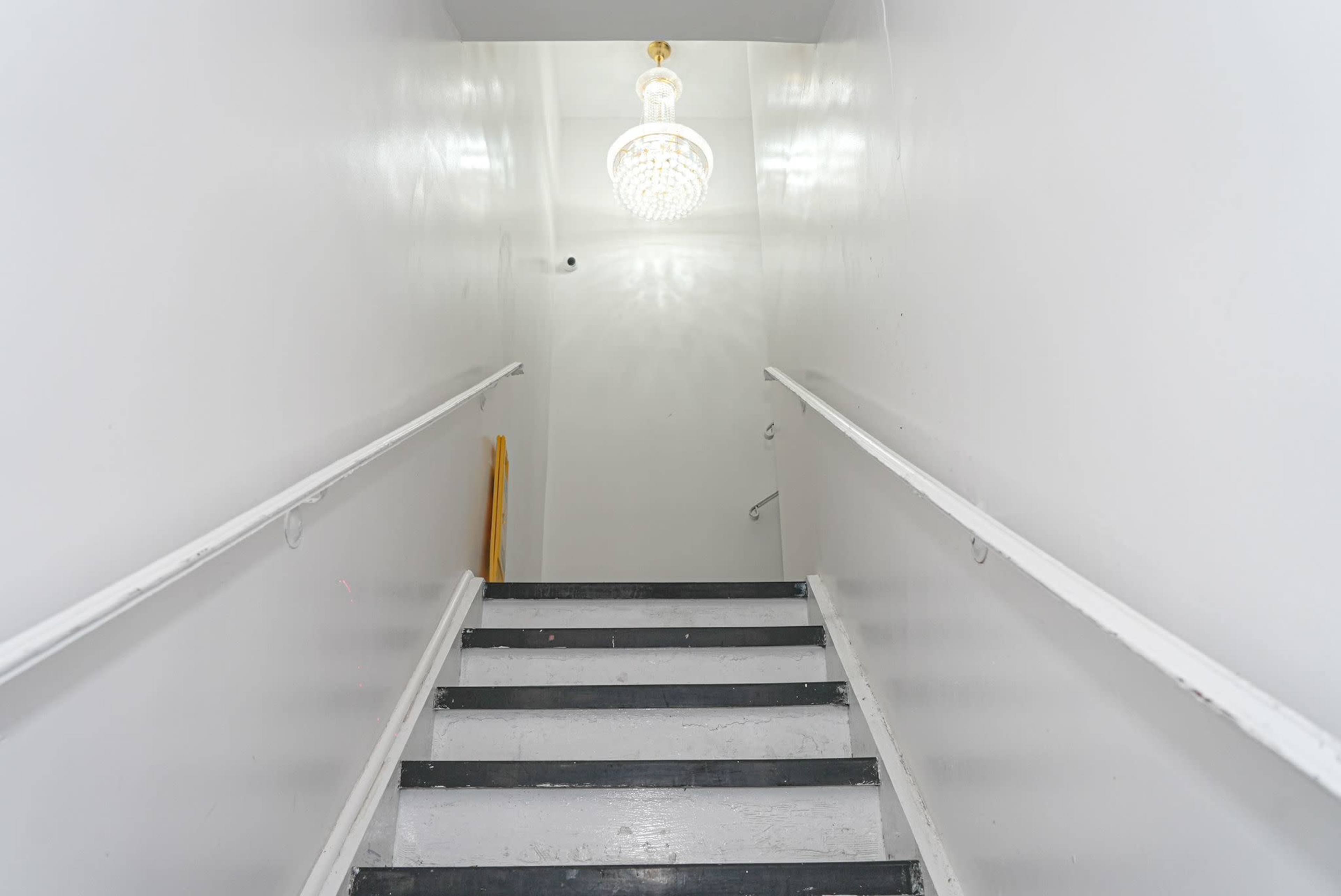 A set of black and white stairs leads upward to a well-lit landing with a chandelier hanging from the ceiling.