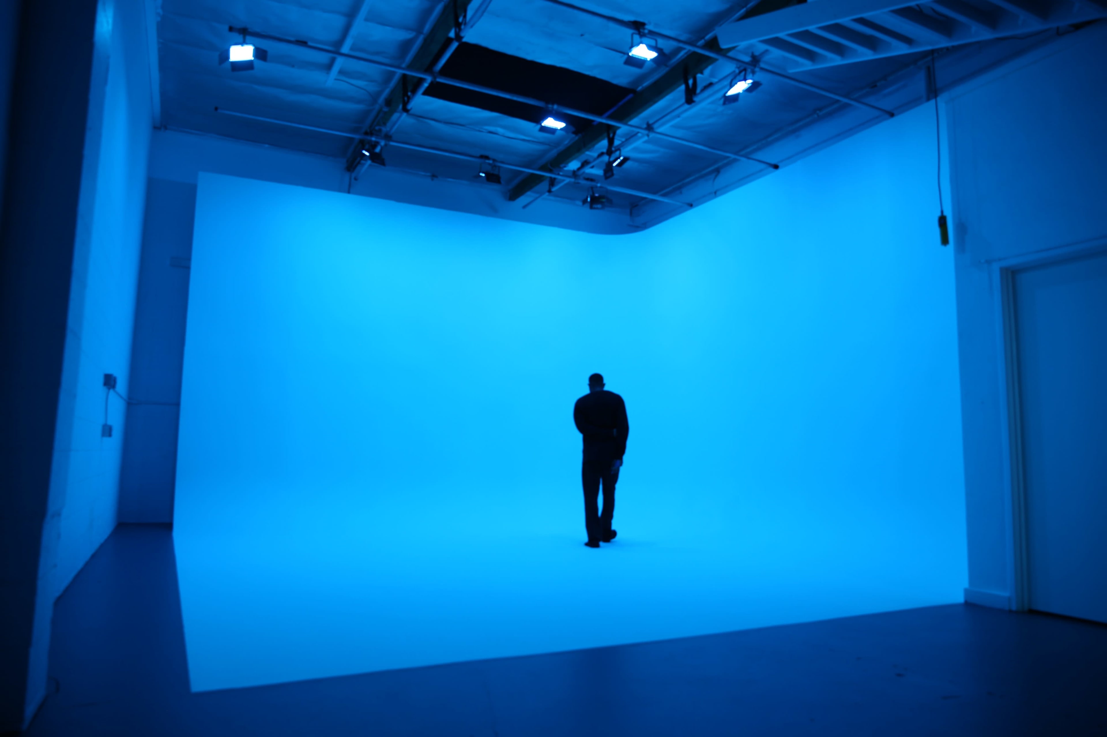 A figure stands alone in a large, brightly lit blue studio with smooth walls and floor.