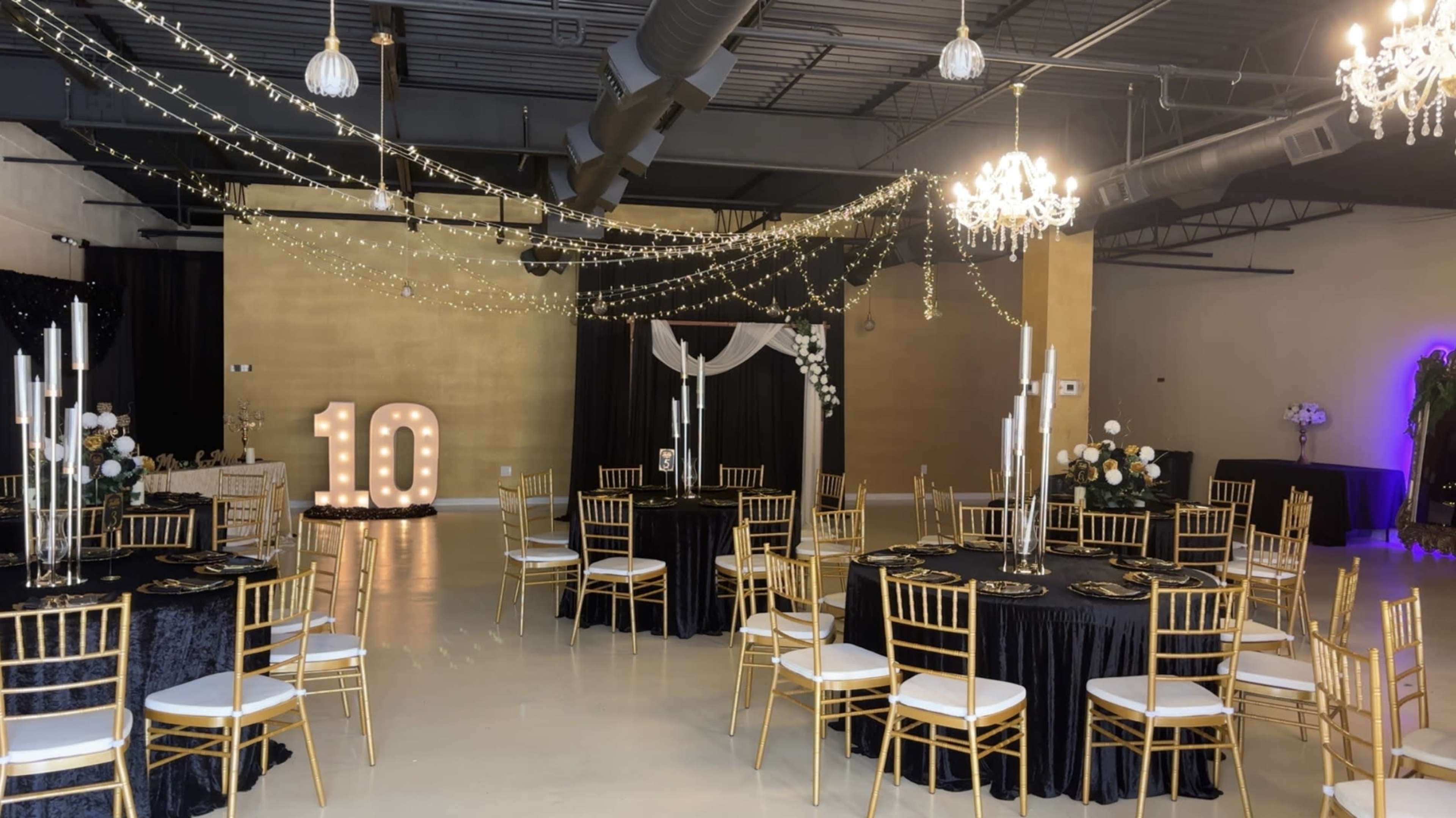 The image shows an elegantly decorated event space with golden walls, black and gold tables set up with white chairs, and a large "10" illuminated display in the background.