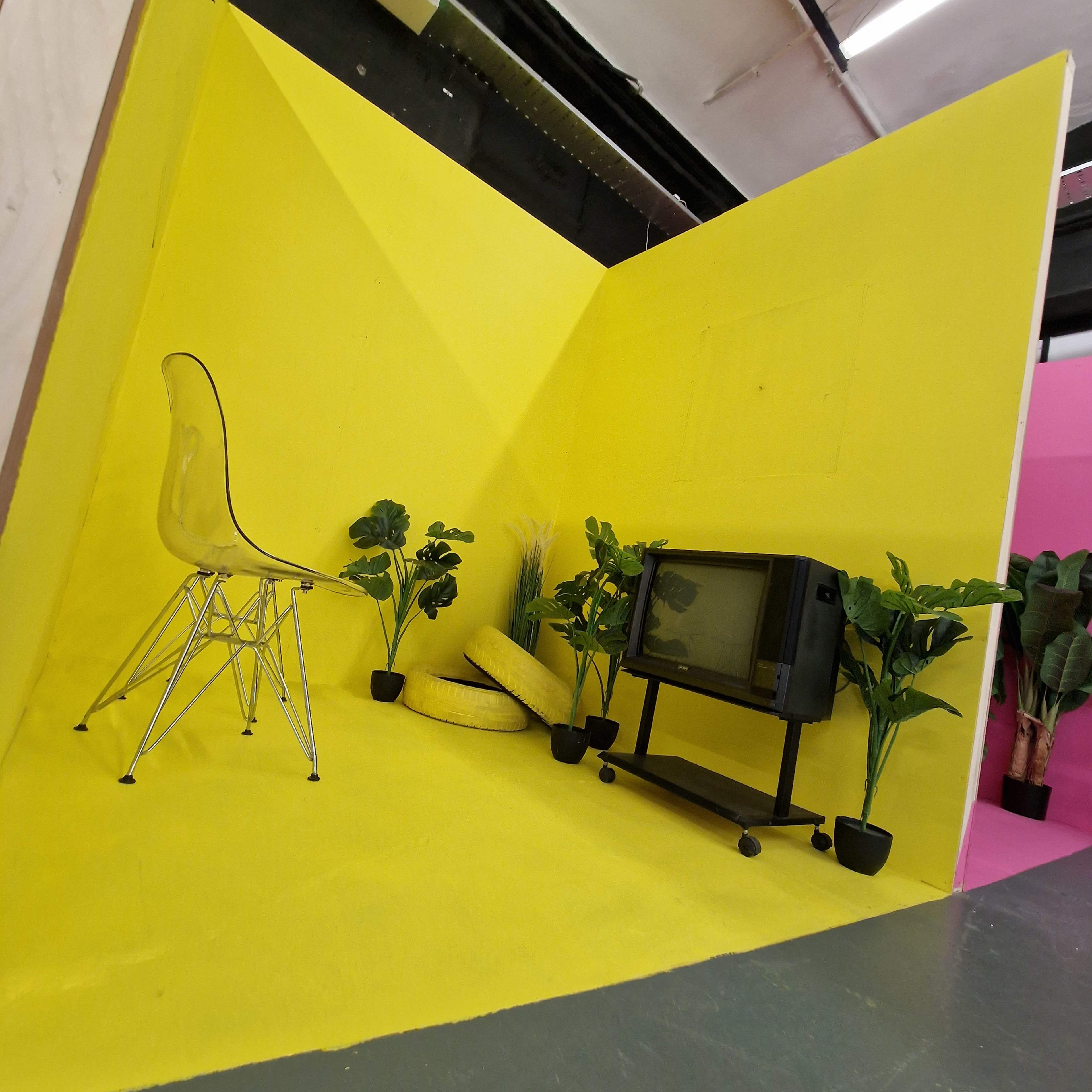 A bright yellow corner space featuring a clear chair, a vintage television on a stand, and several potted plants.