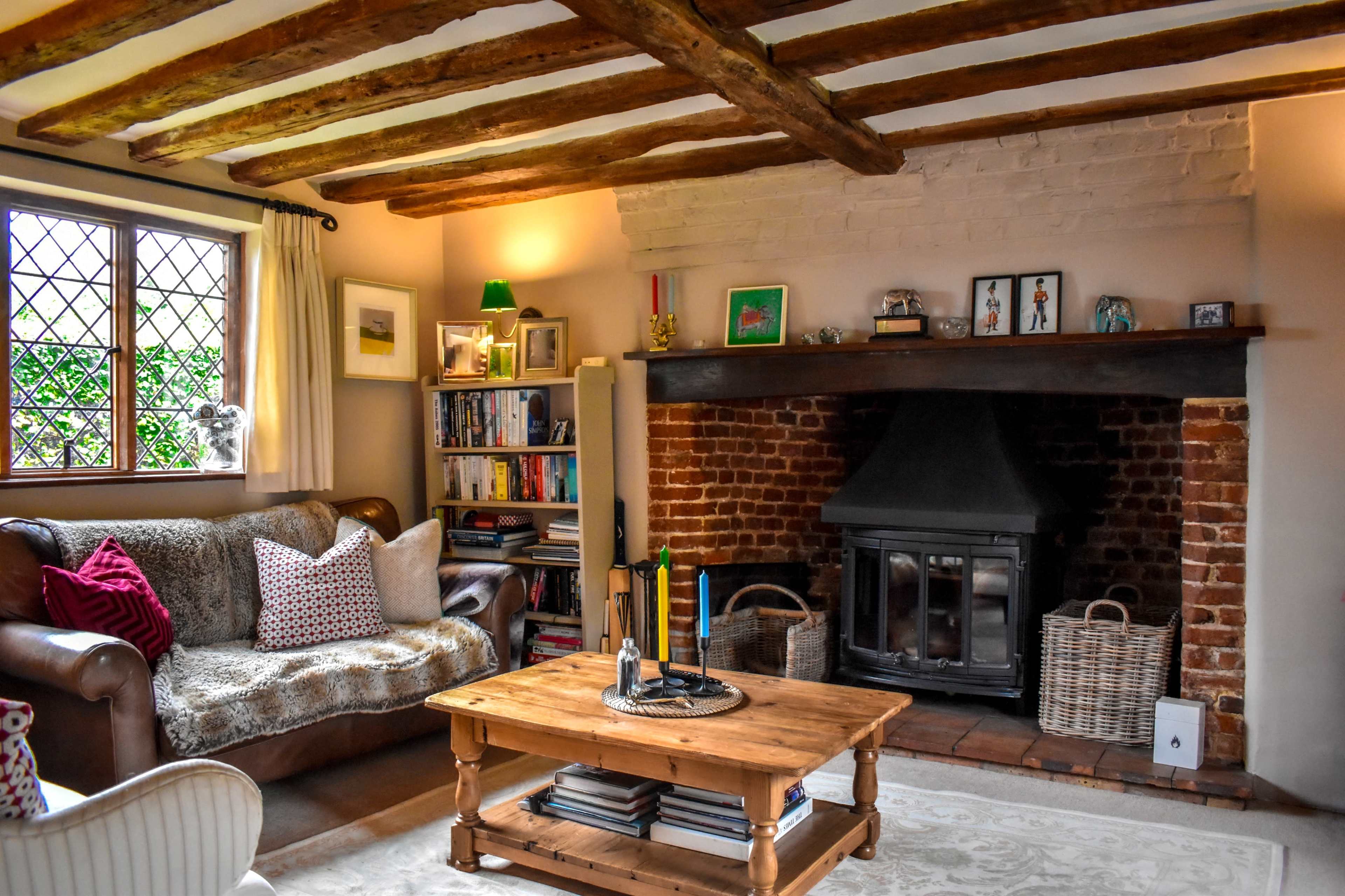 The image shows a cozy living room featuring a sofa, a wooden coffee table, a bookshelf, and a fireplace with brick detailing.