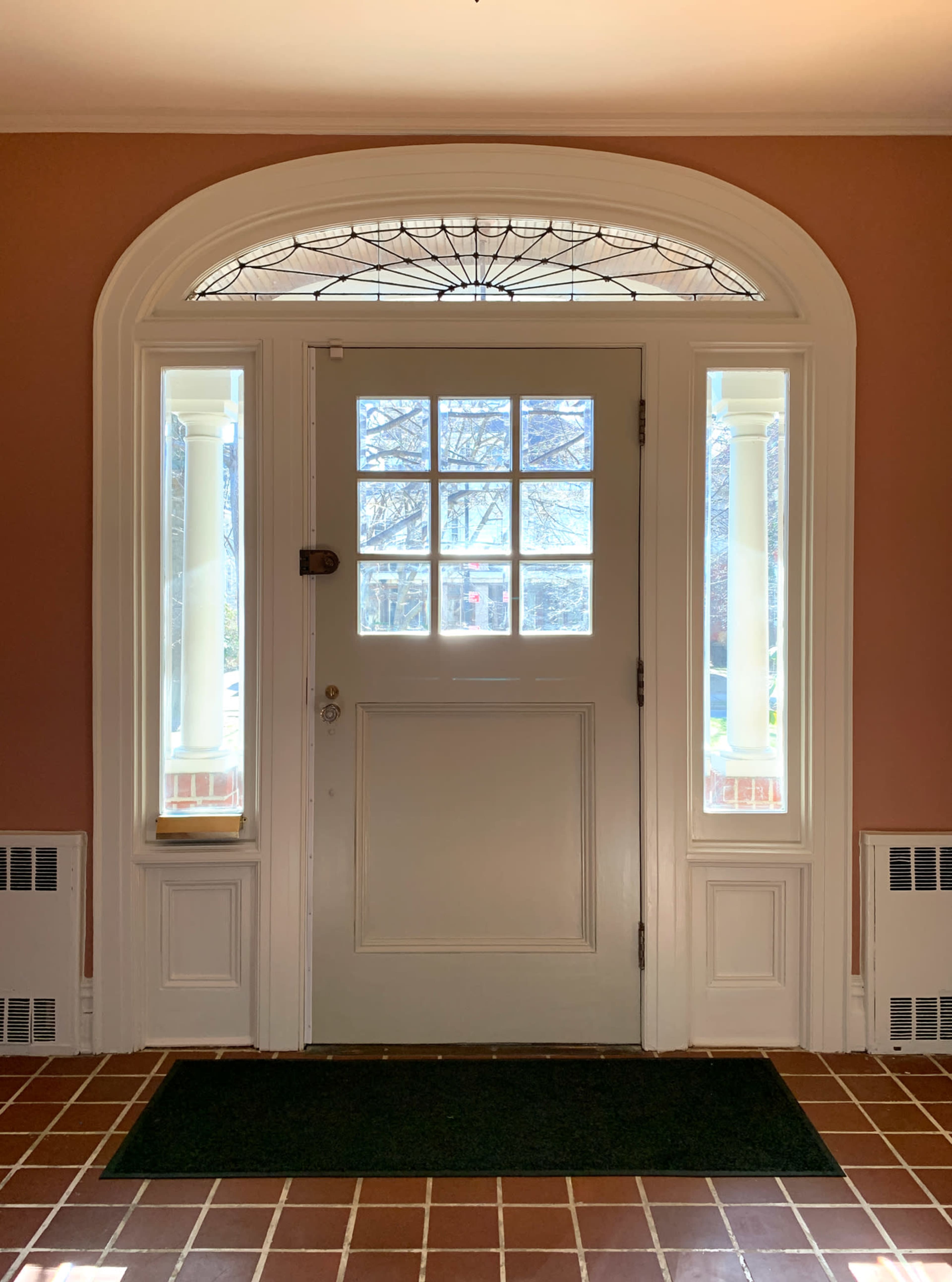 A front door with glass panels on either side, located in a foyer with a tiled floor and a welcome mat.