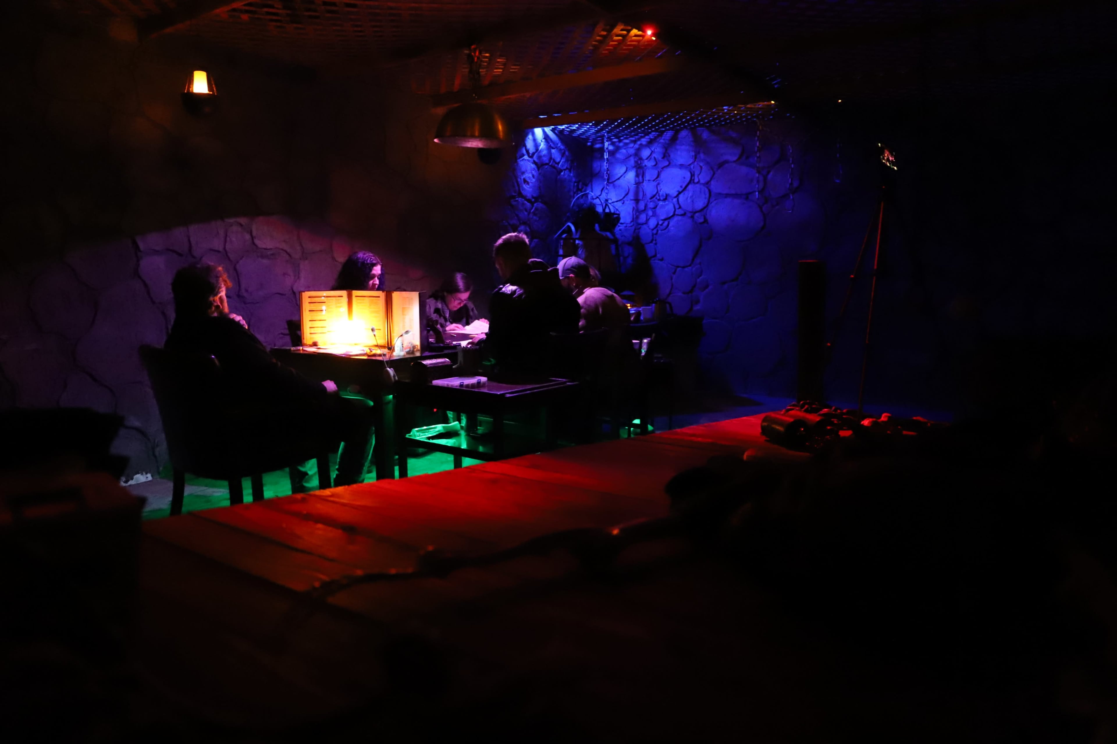 A group of people sit around a dimly lit table in a room with stone walls, engaged in conversation.