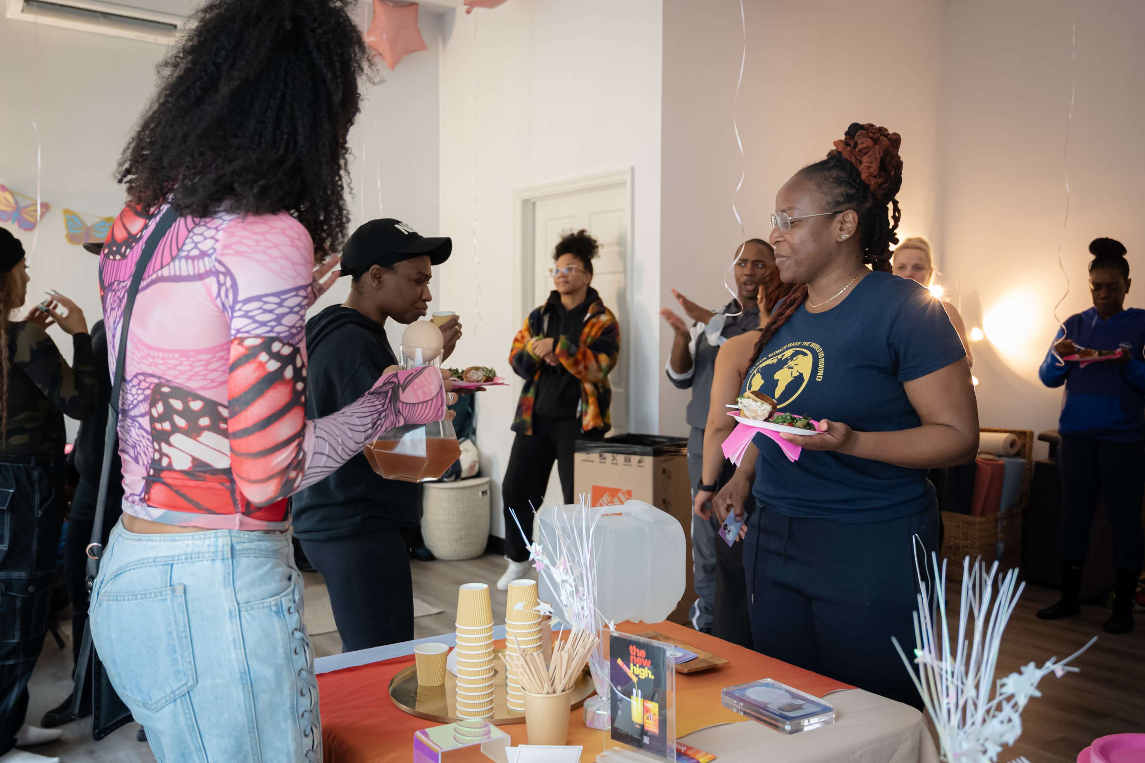 A group of people is gathered in a brightly lit room, socializing and enjoying food during an event.