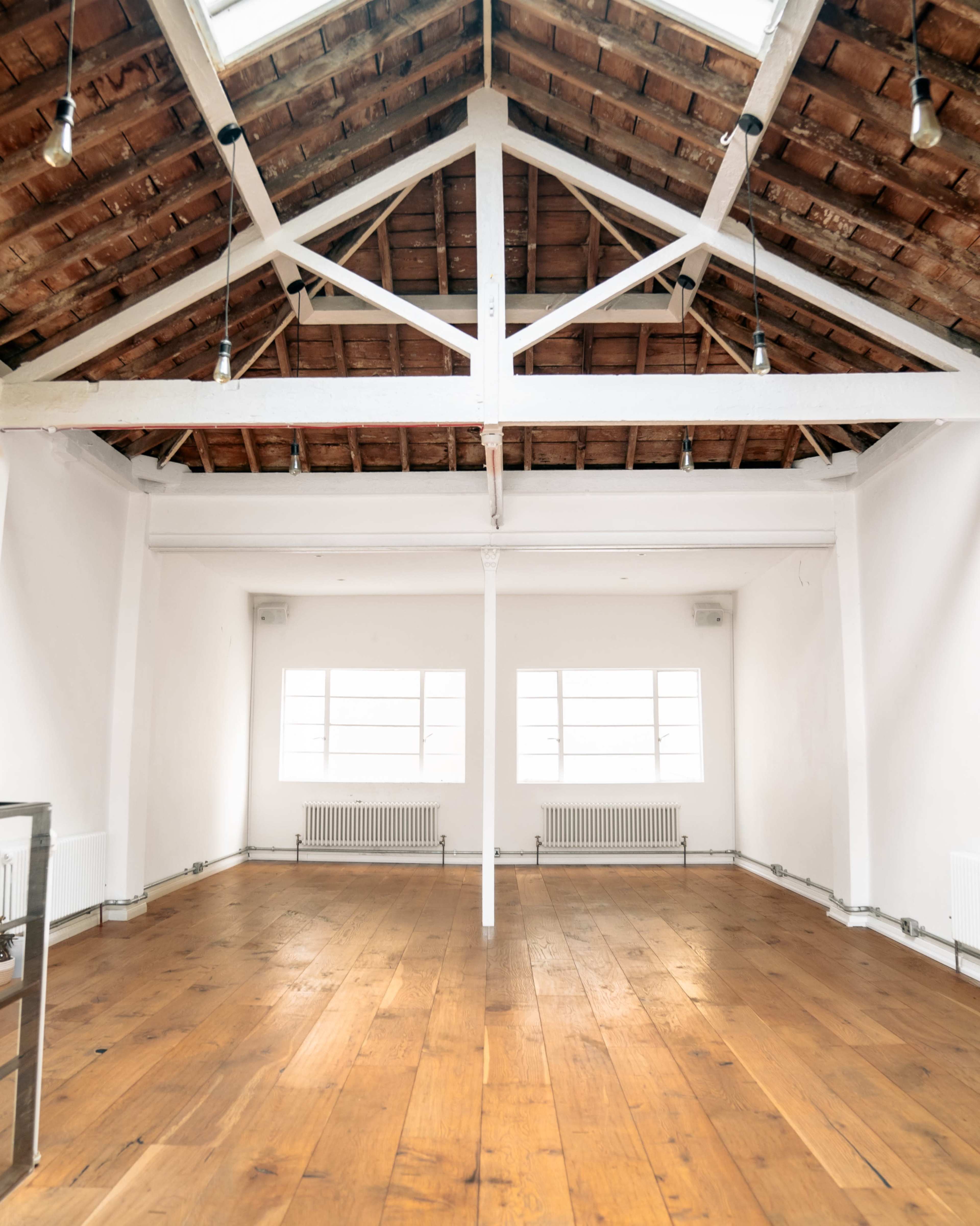 A spacious, empty loft with a high wooden ceiling and large windows allowing natural light to enter.