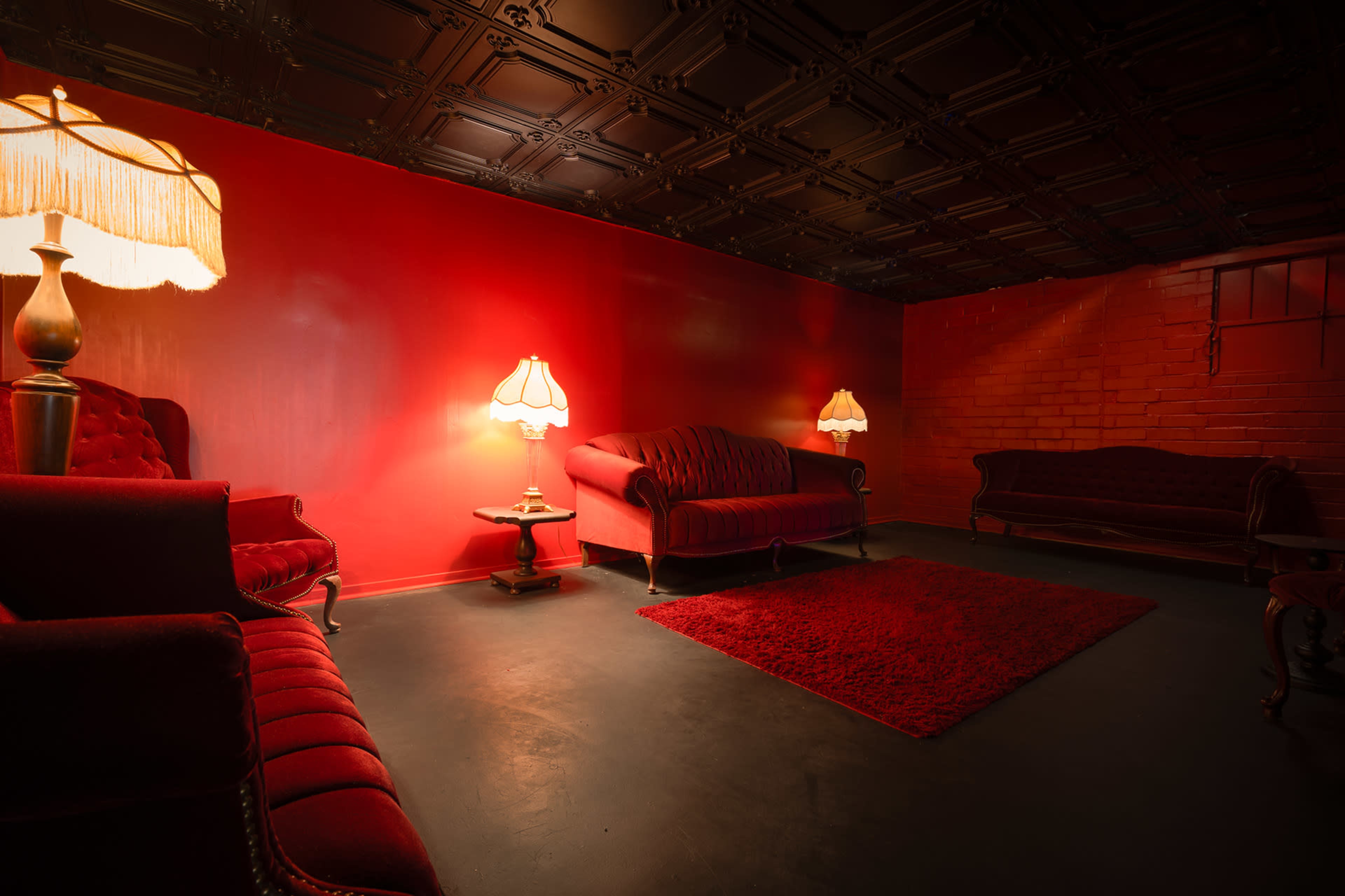 The room features red walls, dark flooring, and matching red furniture, with two lamps providing soft lighting.