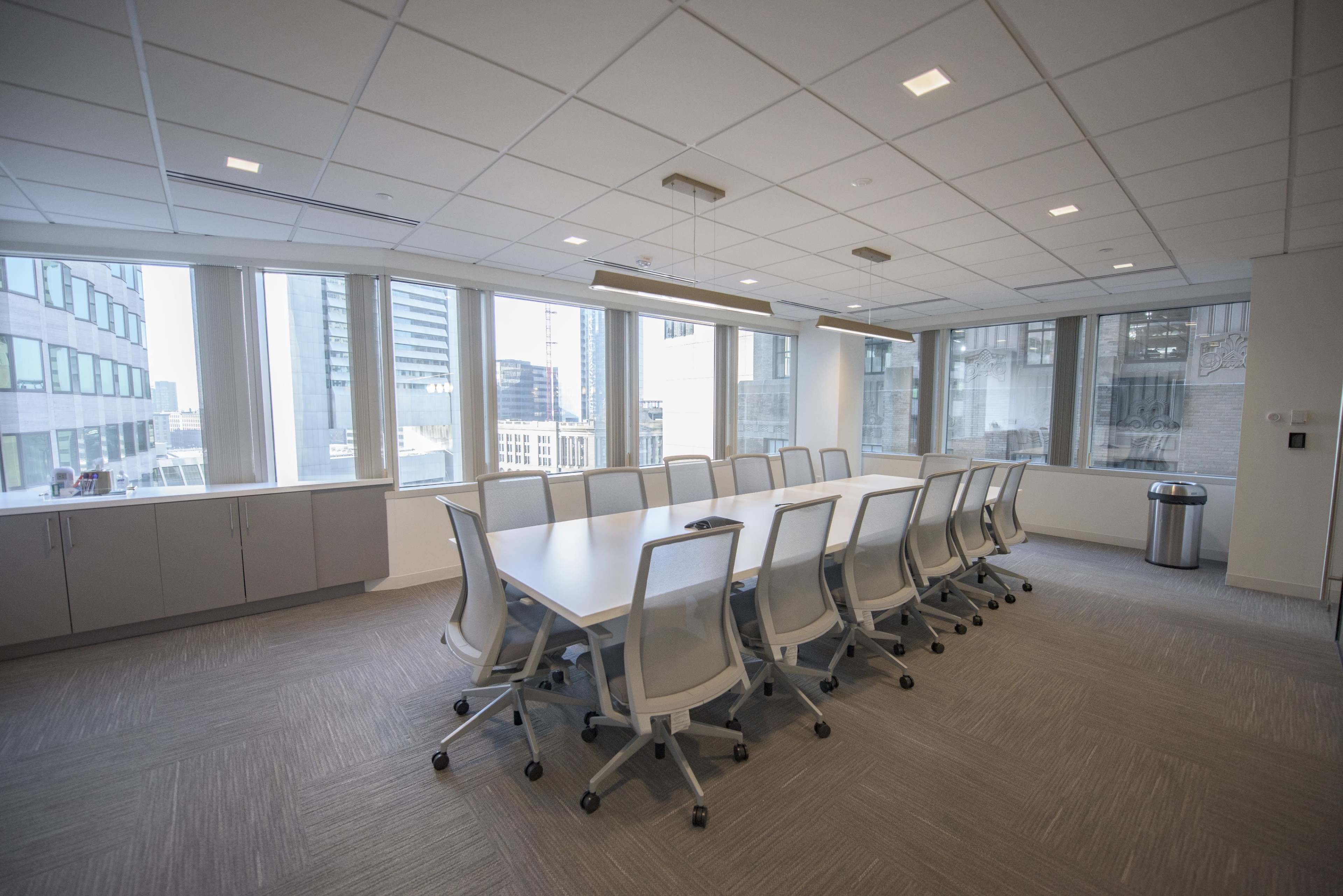 A large conference room features a long table surrounded by ergonomic chairs, with floor-to-ceiling windows offering a city view.