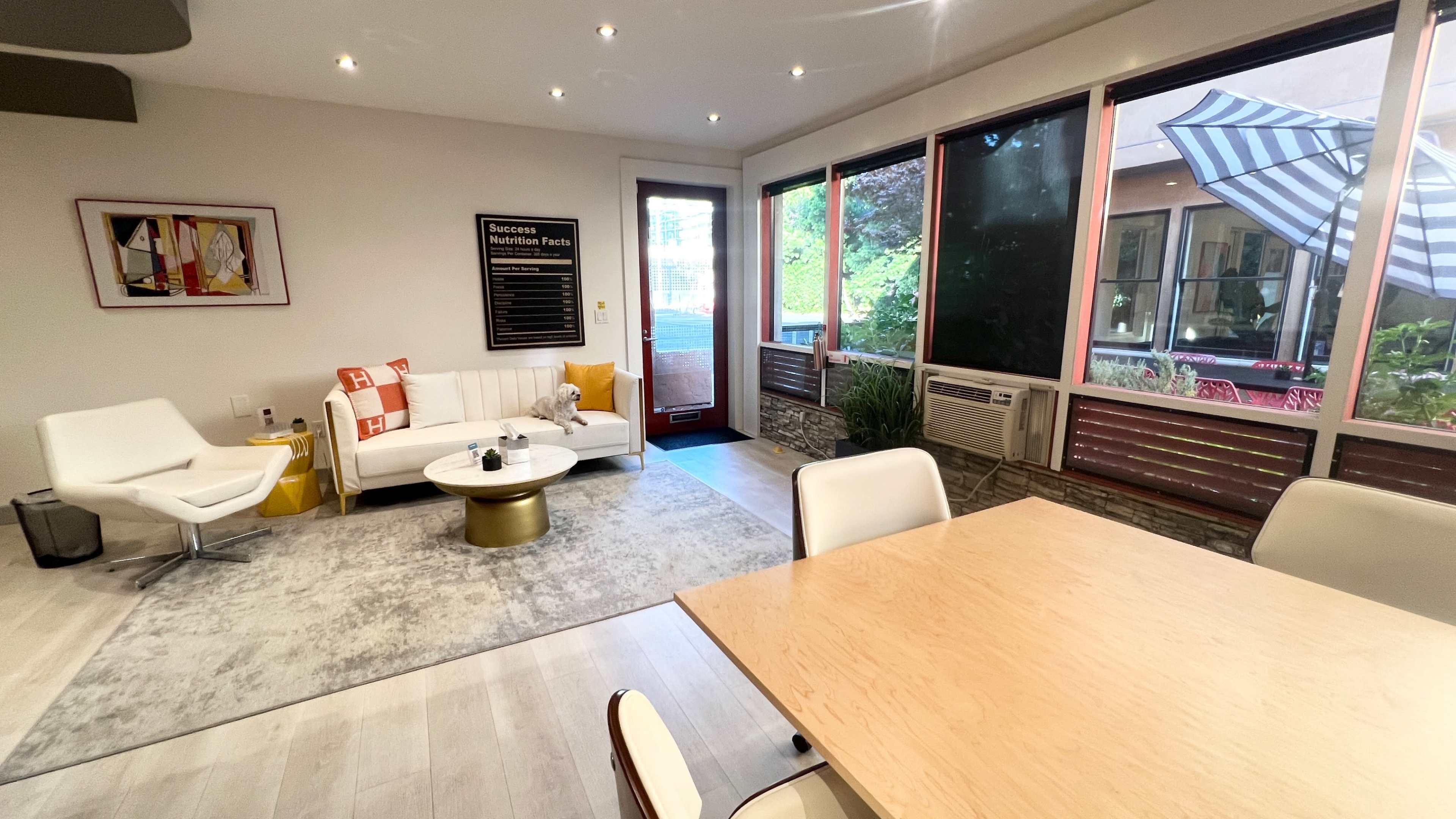 A modern living space with a white sofa, a round coffee table, and large windows that provide views of an outdoor patio.
