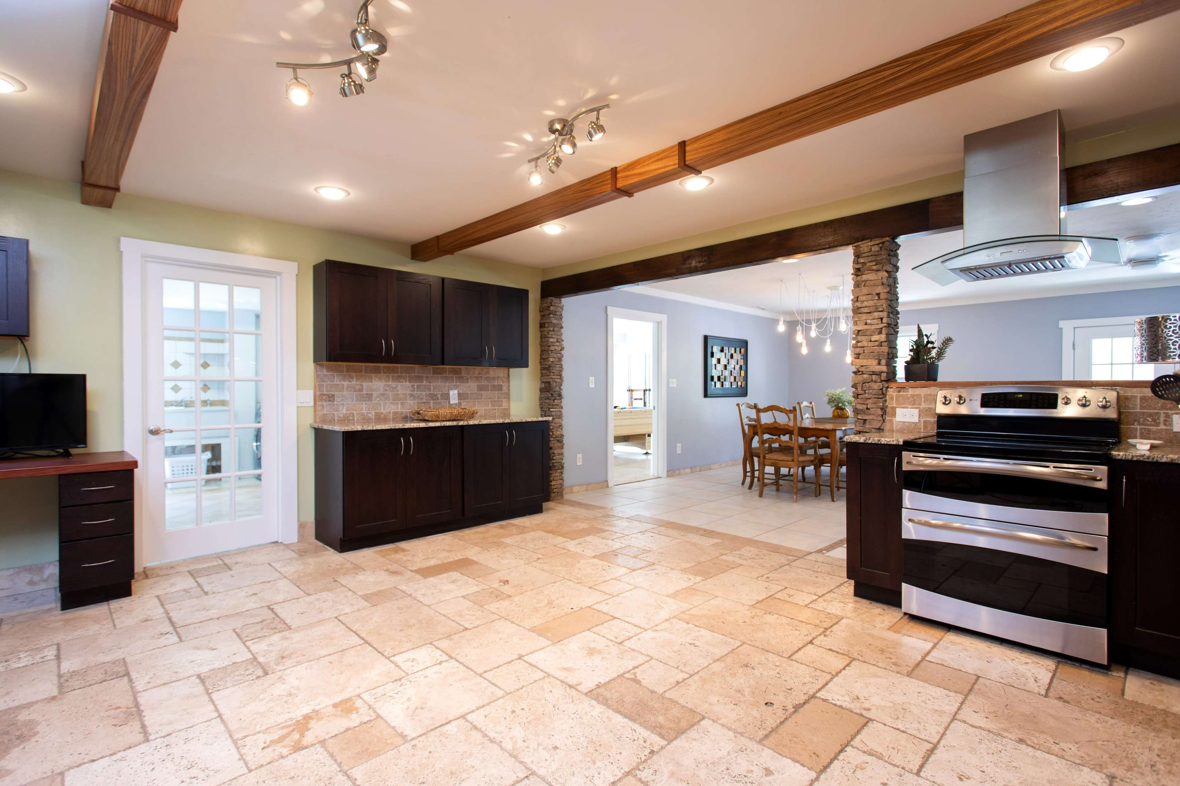 An open-concept kitchen and dining area with wooden beams, stone accents, and tiled flooring.