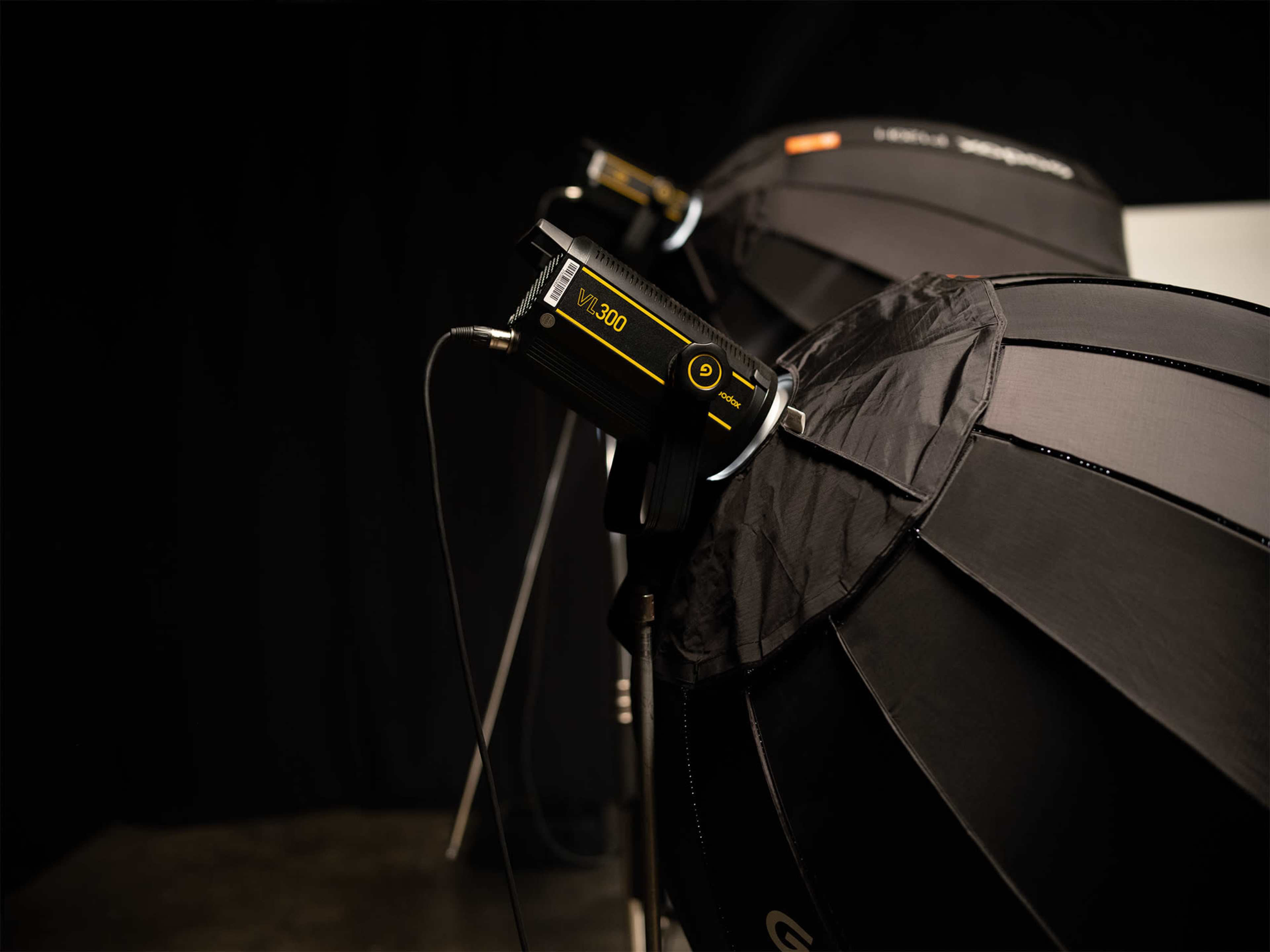 The image features two studio light setups with softboxes attached, positioned in a darkened environment.