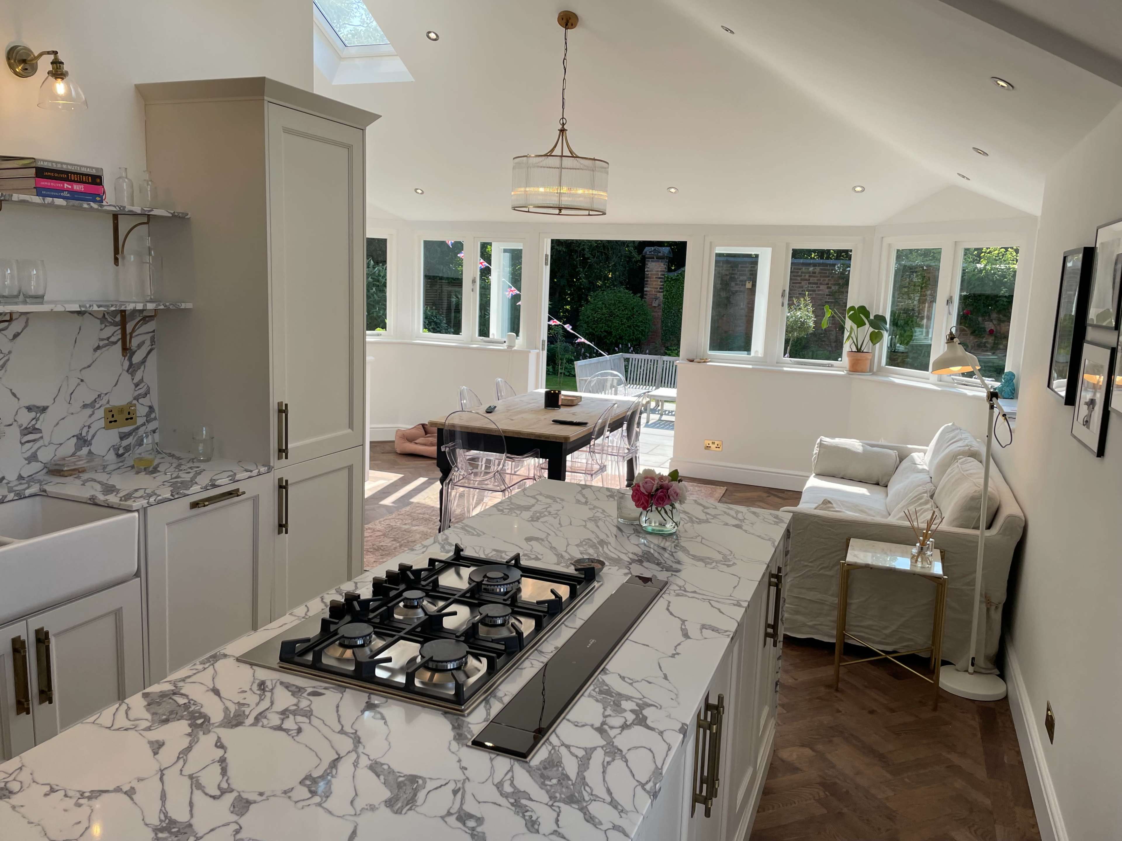A modern kitchen and living space with a marble countertop, gas stove, and large windows allowing natural light to fill the room.