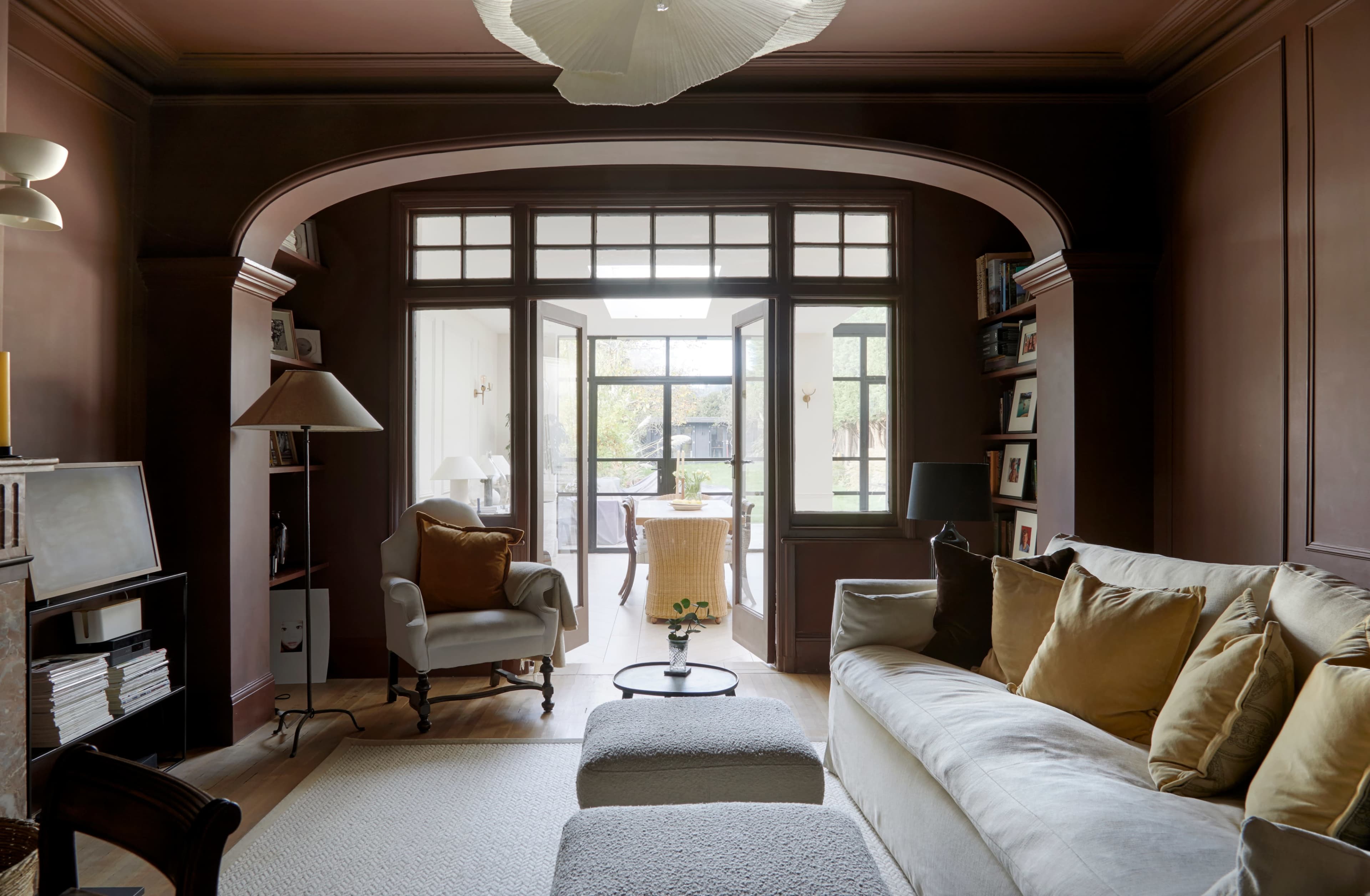 The image shows a cozy living room with a light-colored sofa, a small coffee table, and arched doorways leading to a brightly lit dining area.