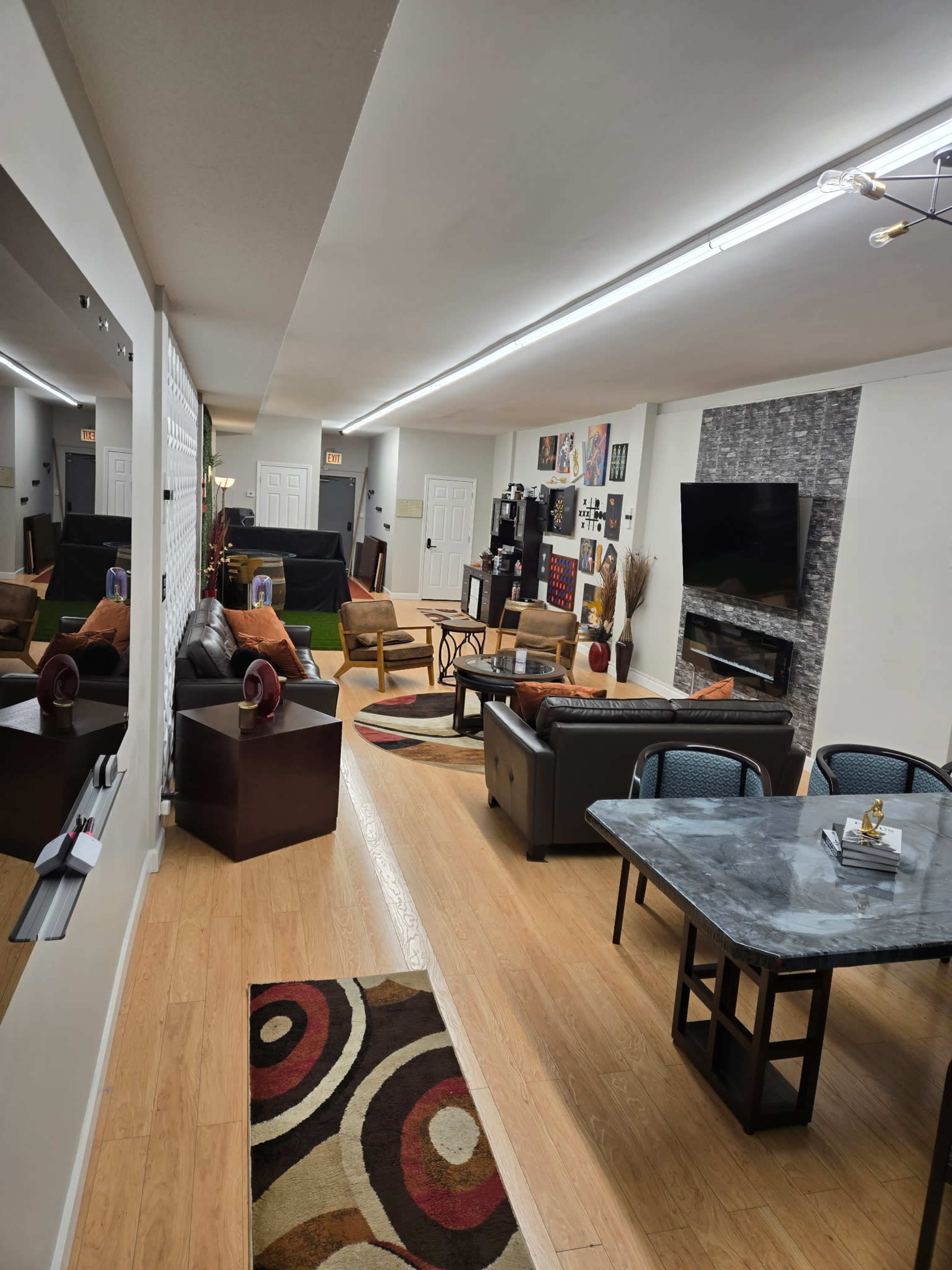 The image shows a modern, open living space with a combination of seating areas, a dining table, and decorative wall elements.