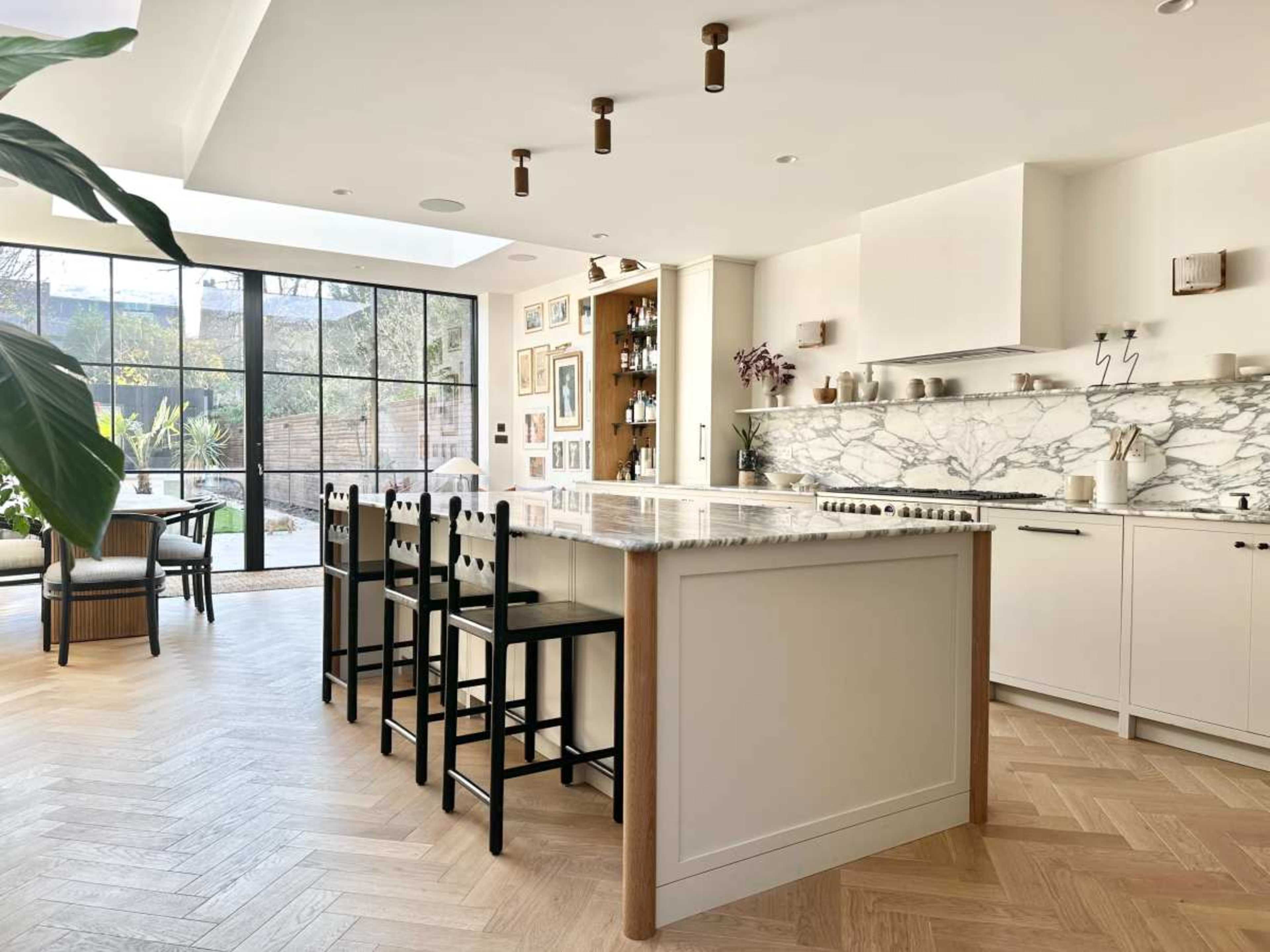 The image shows a modern kitchen with a marble countertop and island, surrounded by a large window that opens to a garden.