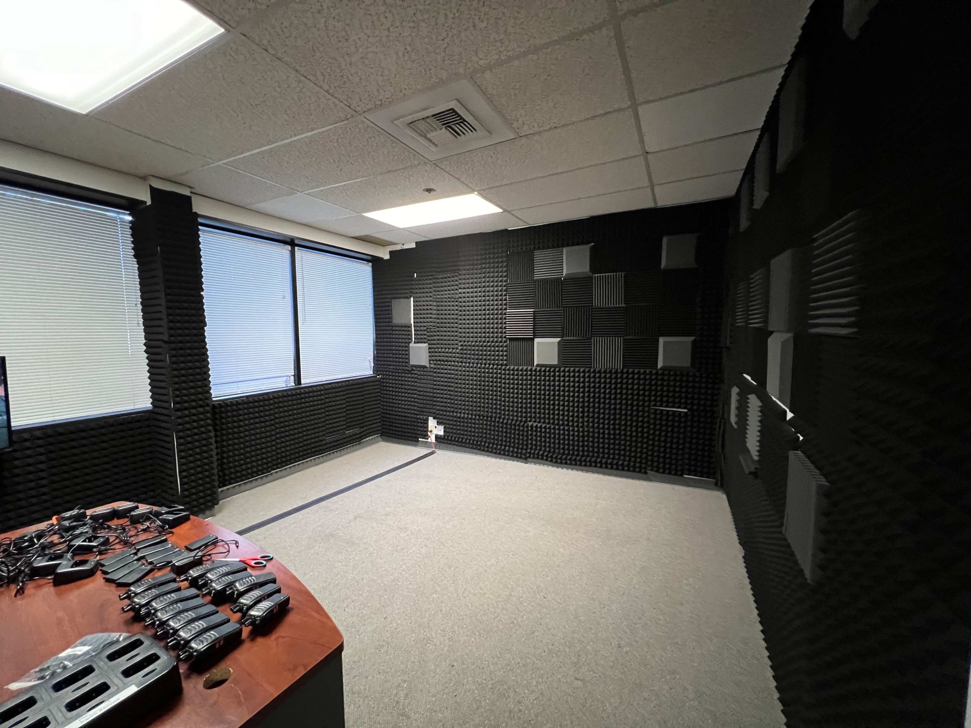 A soundproof room with black acoustic foam panels on the walls, a gray carpet, and a table displaying various tools or equipment.