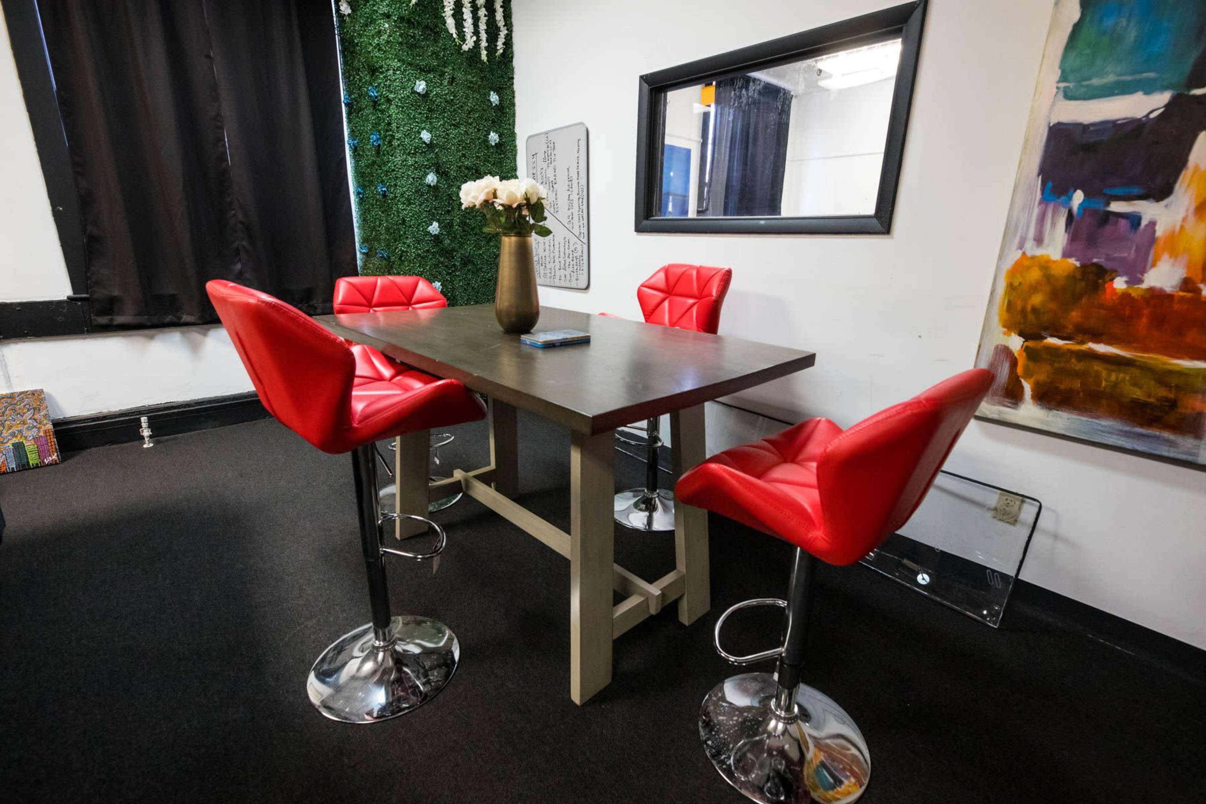 A modern dining area featuring a rectangular table surrounded by four red bar stools and decorated with a vase of flowers.