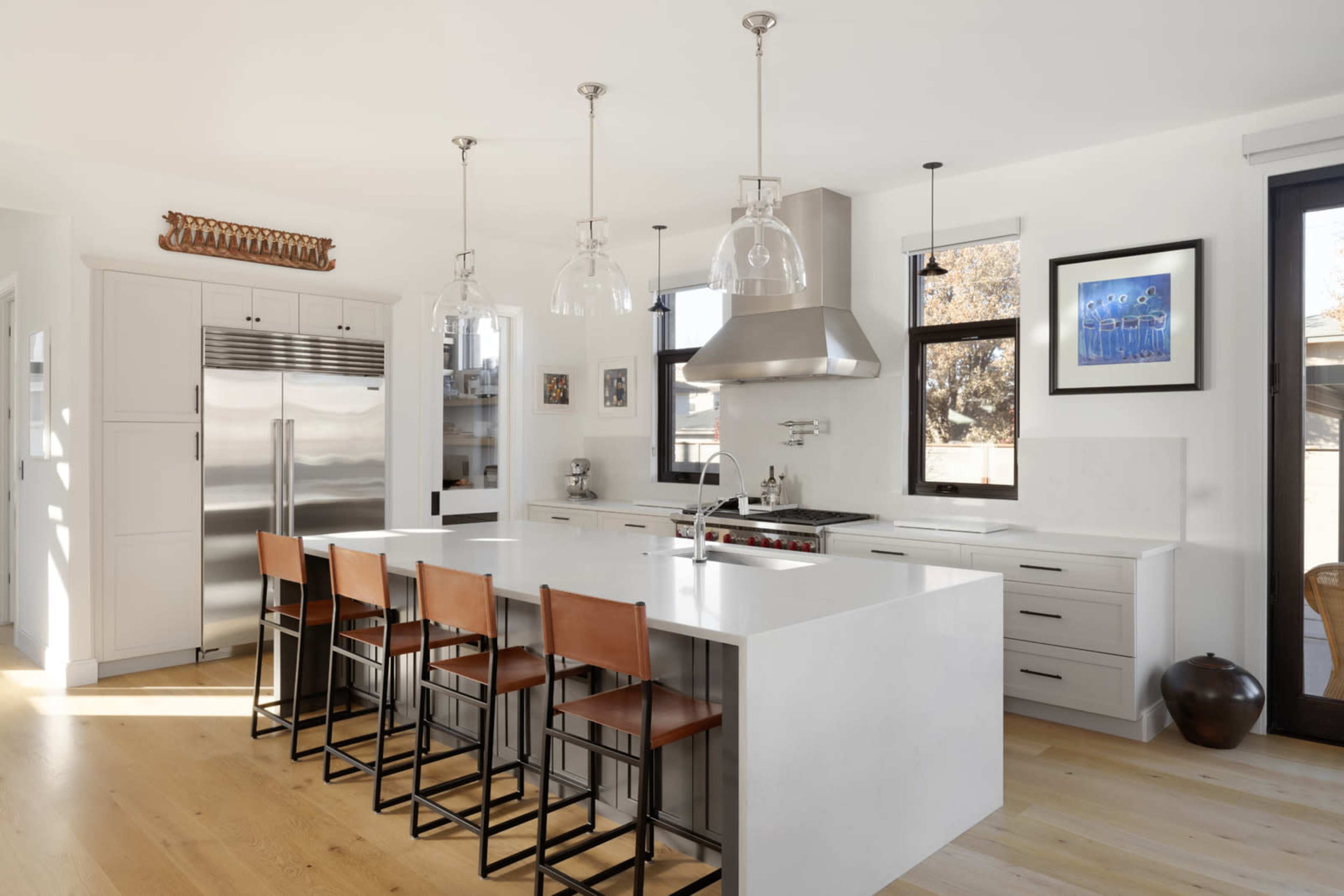 The image features a modern kitchen with a large white island, stainless steel appliances, and bar stools positioned along one side.