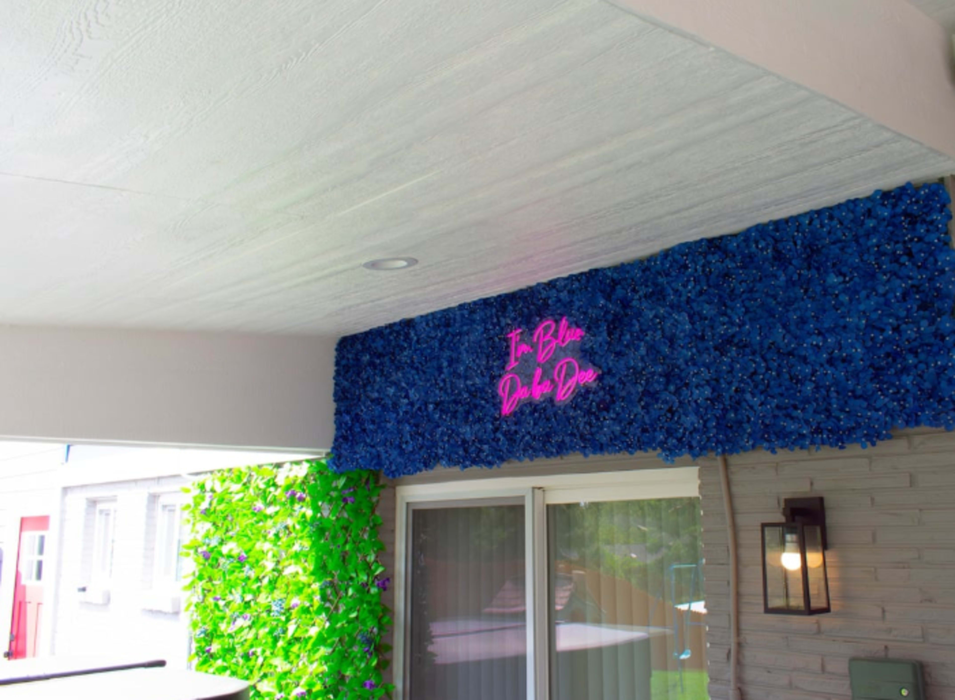 A decorative wall featuring blue flowers and a pink neon sign that reads "In Blue Da Ba Dee."