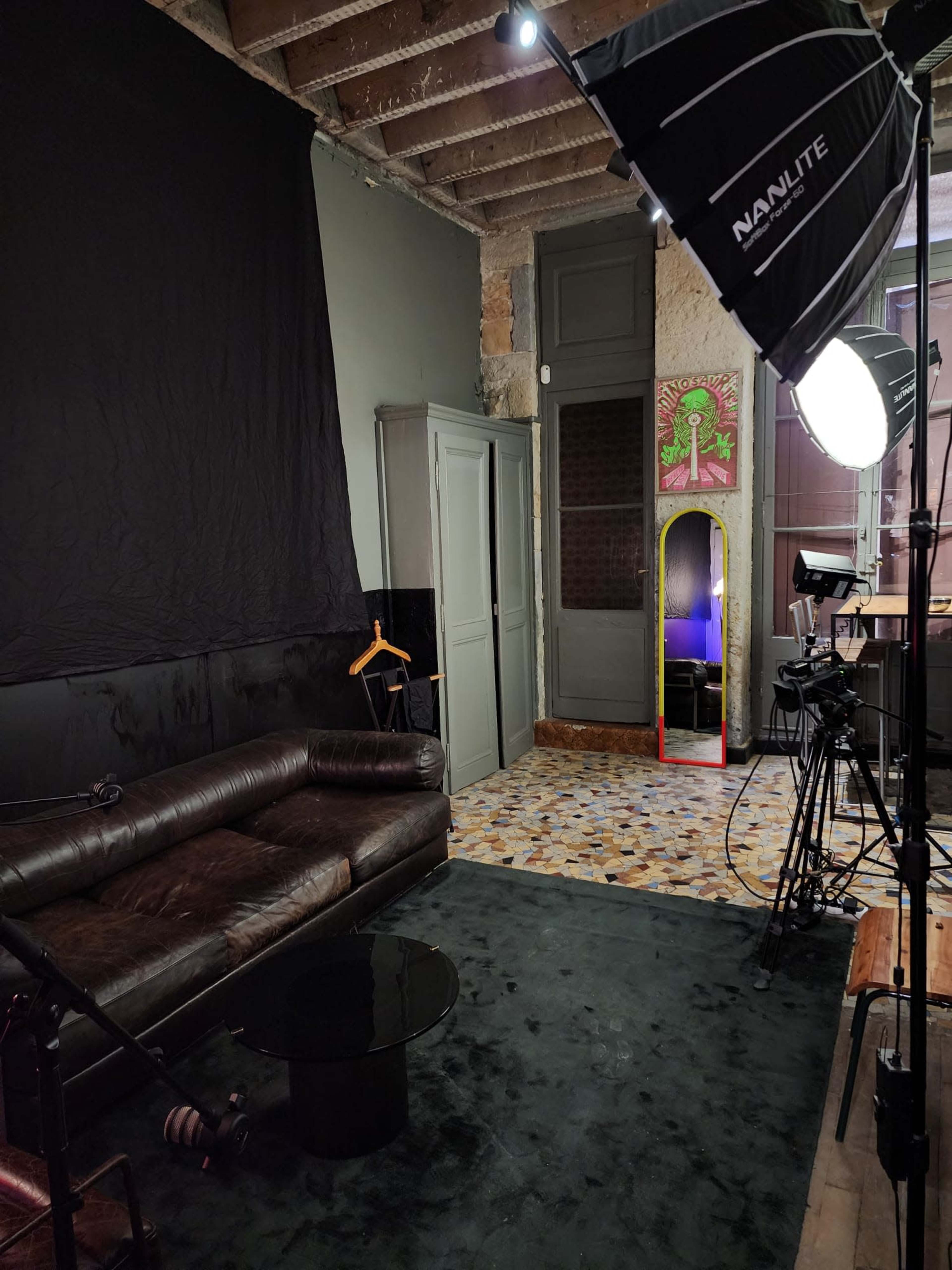 A room with a leather sofa, a black backdrop, a mirror with a red frame, and photography equipment.