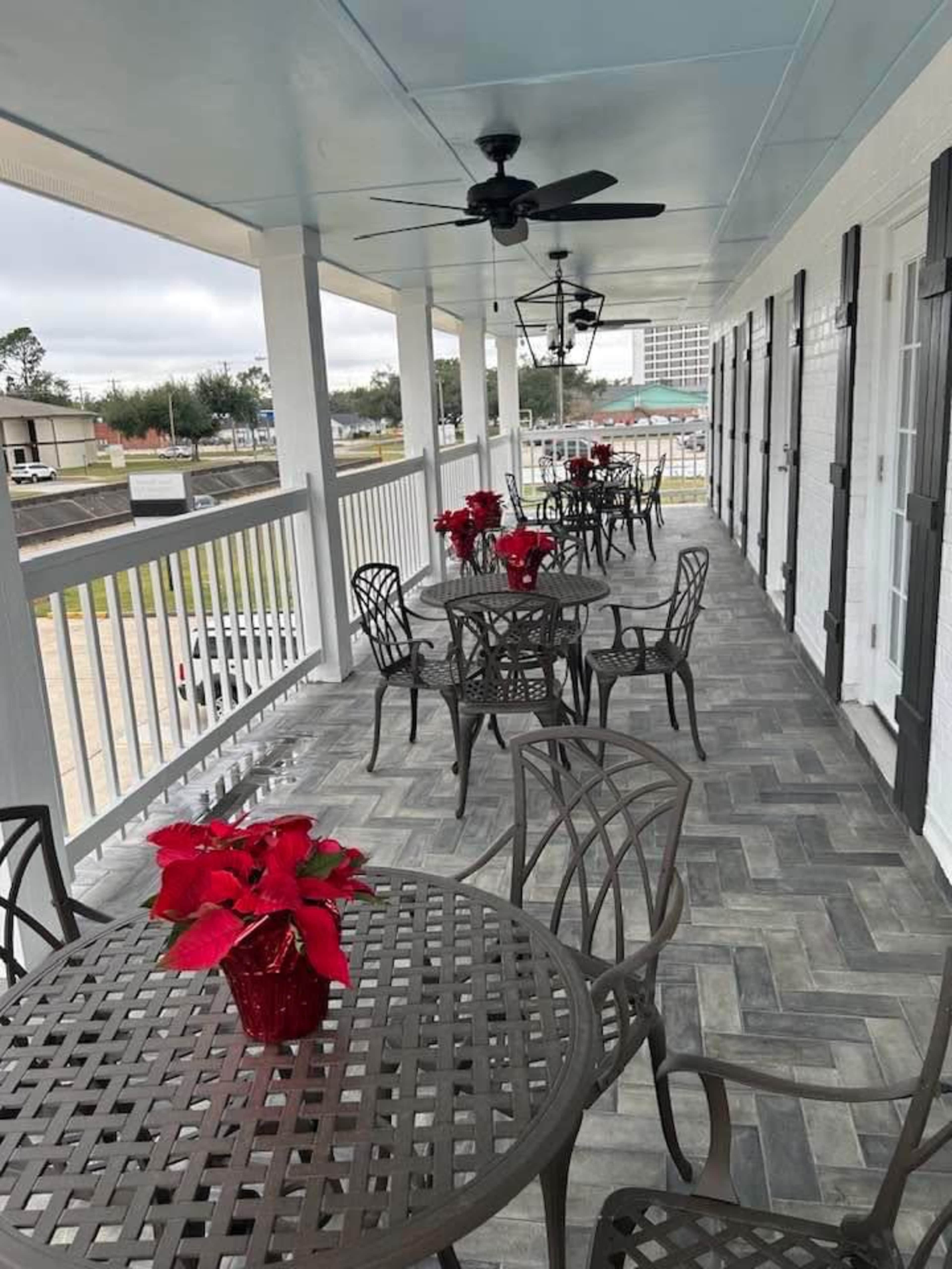 A covered balcony with several round tables and chairs, each adorned with red poinsettia plants.