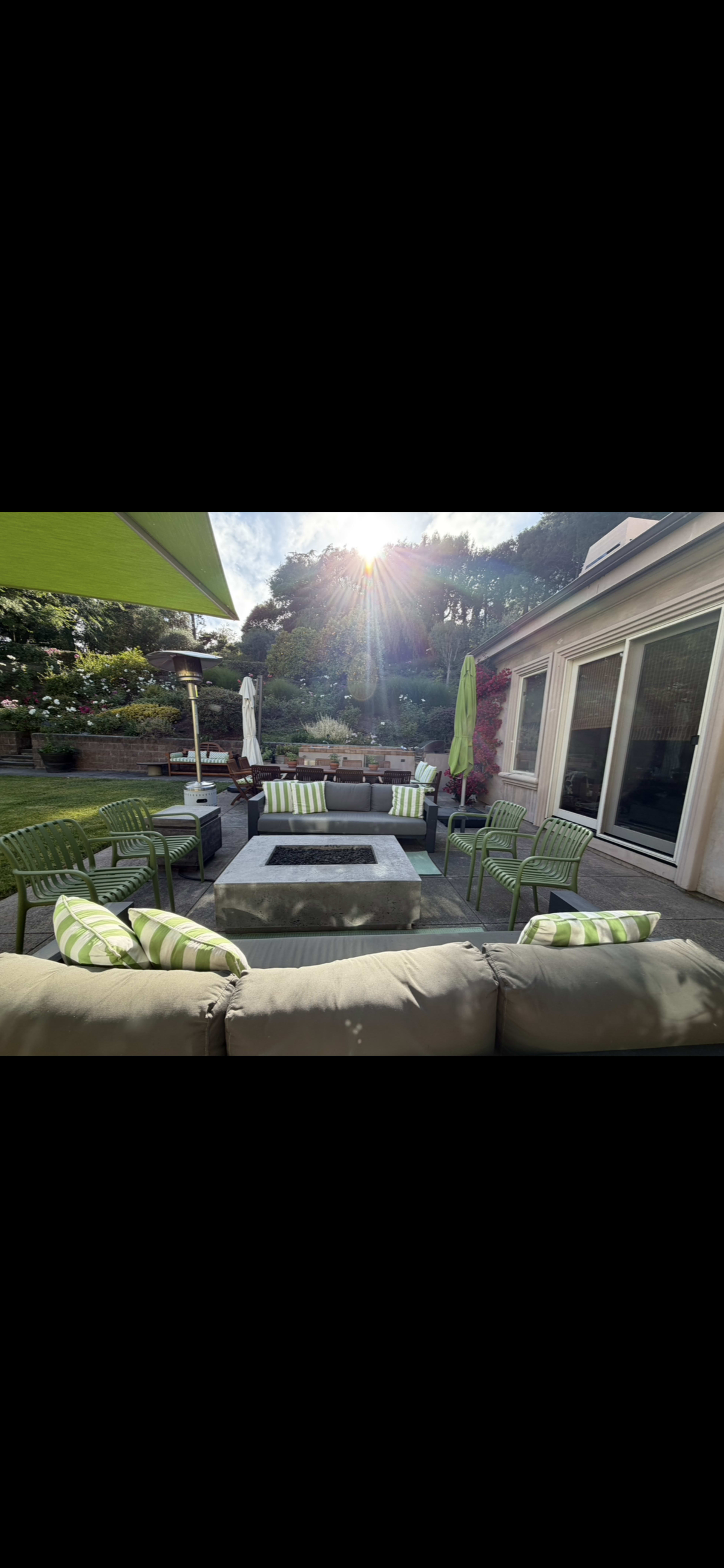 A patio area features green and white striped cushions on lounging chairs and a coffee table, with sunlight shining in the background.
