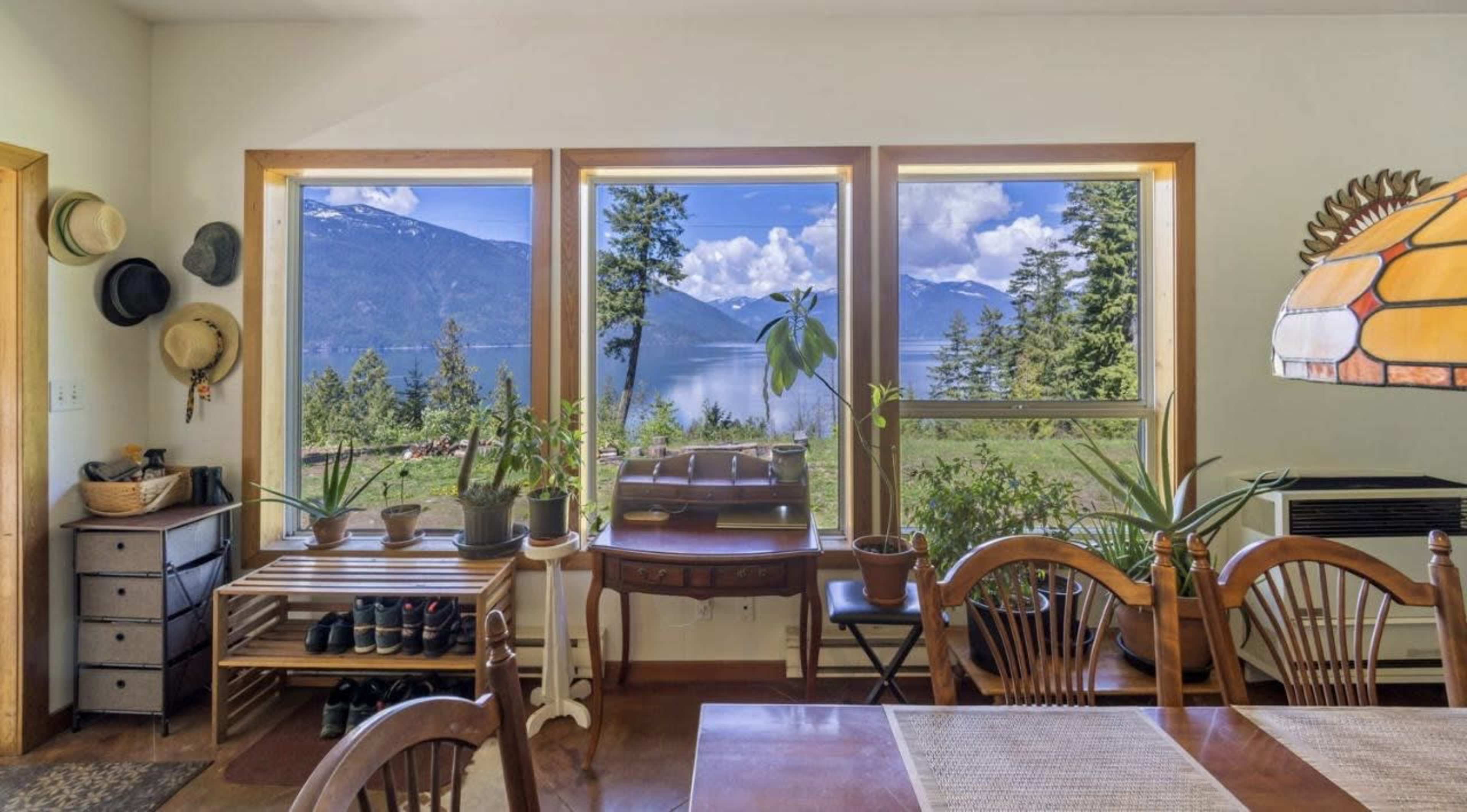 A dining area features a large window with views of a lake surrounded by trees and mountains.