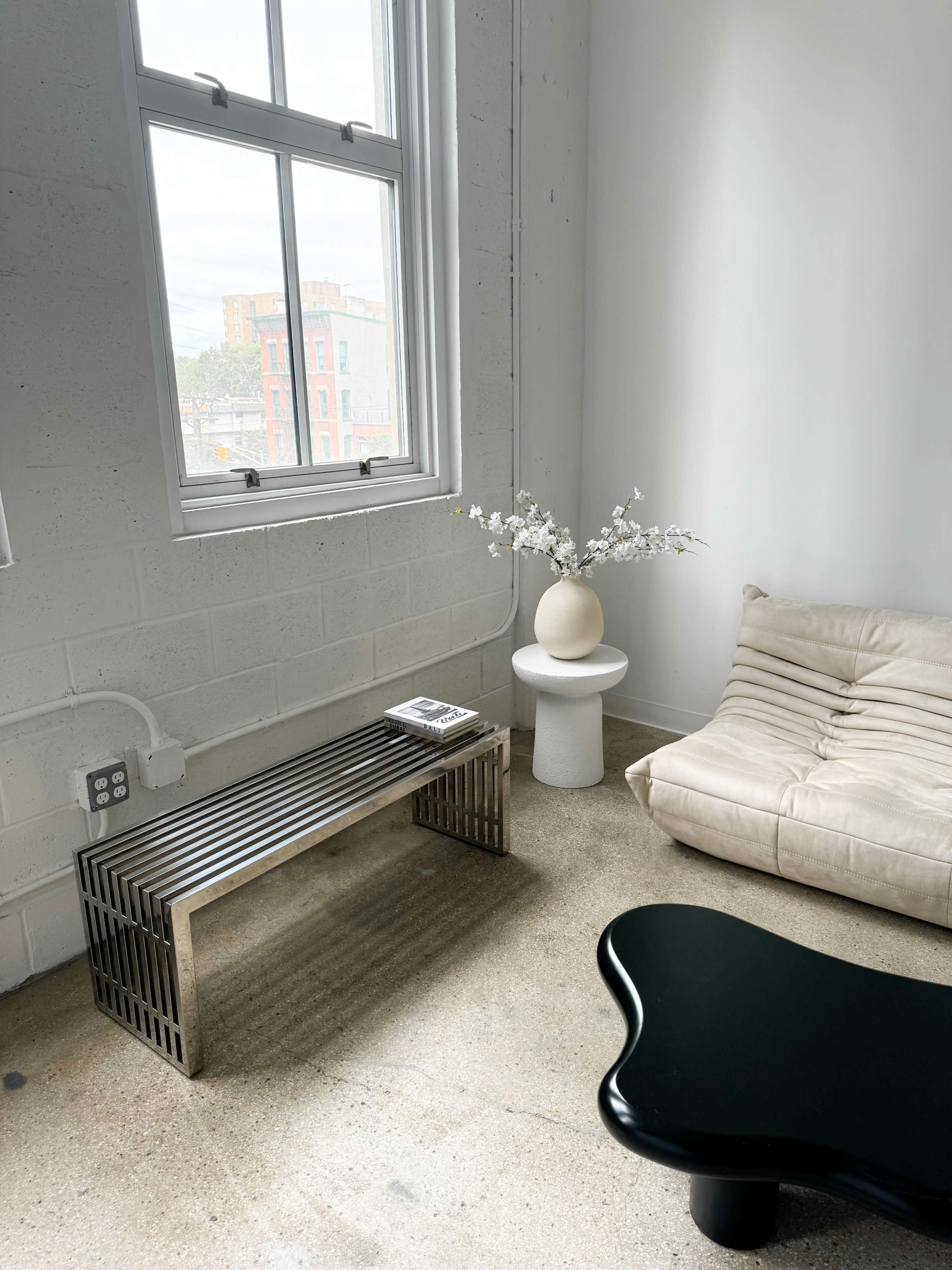 A modern living space features a light-colored sofa, a sleek metal coffee table, and a round side table with a decorative vase and flowers beside a window.