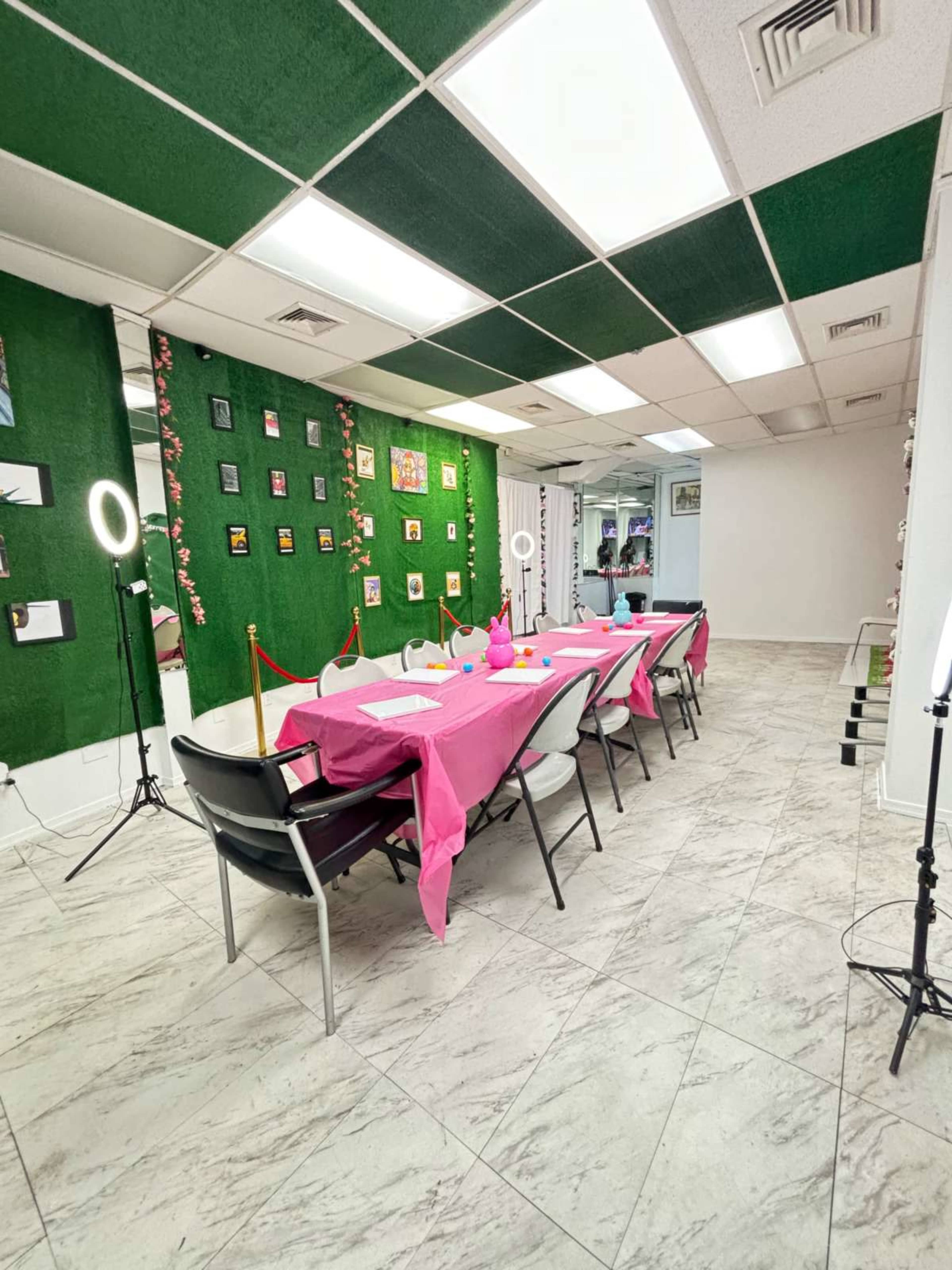 A long table covered with a pink cloth is set up in a brightly lit room, surrounded by decorations on the walls and lighting equipment.