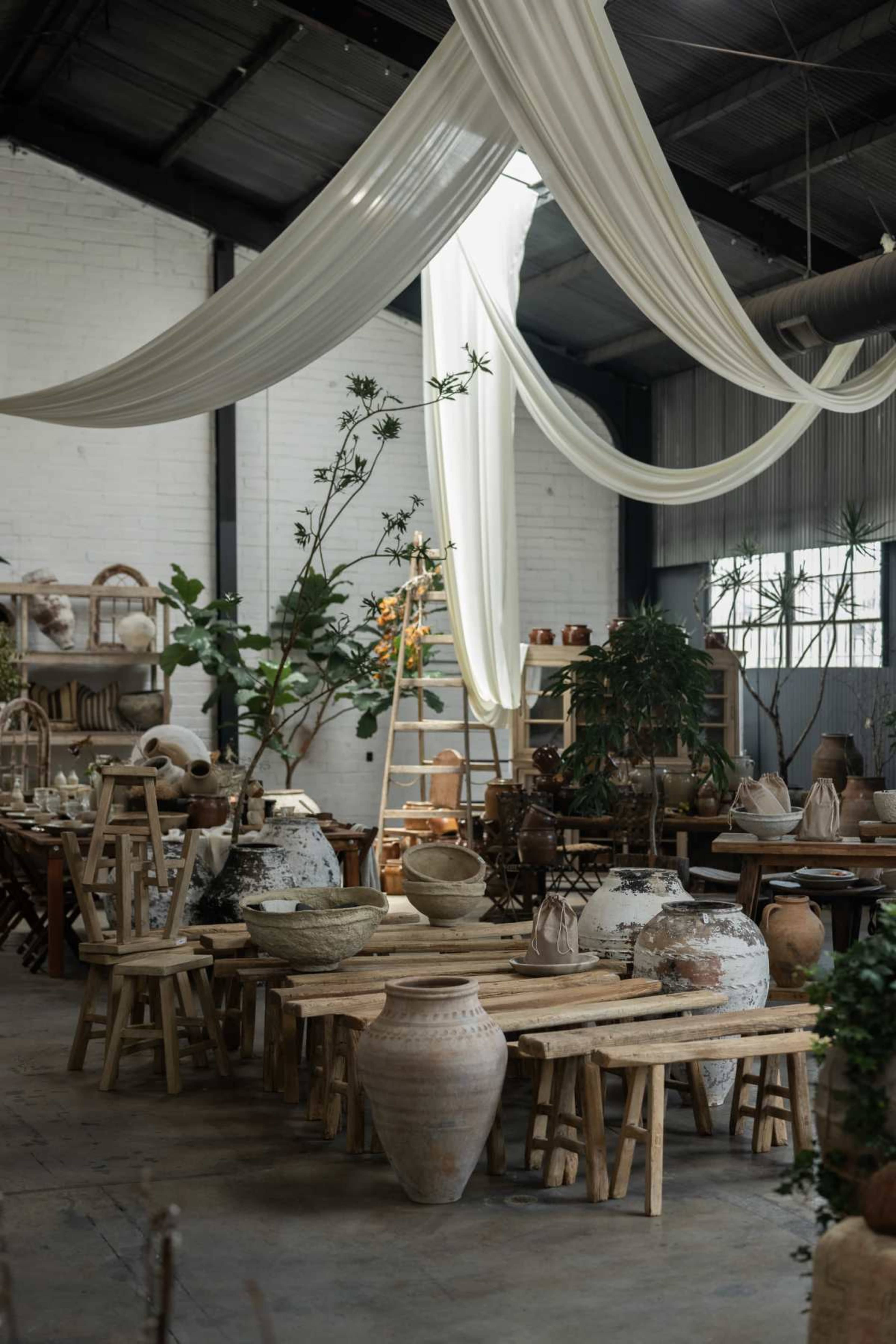 The scene shows a rustic interior filled with various pottery pieces and wooden furniture, illuminated by natural light filtering through the windows.