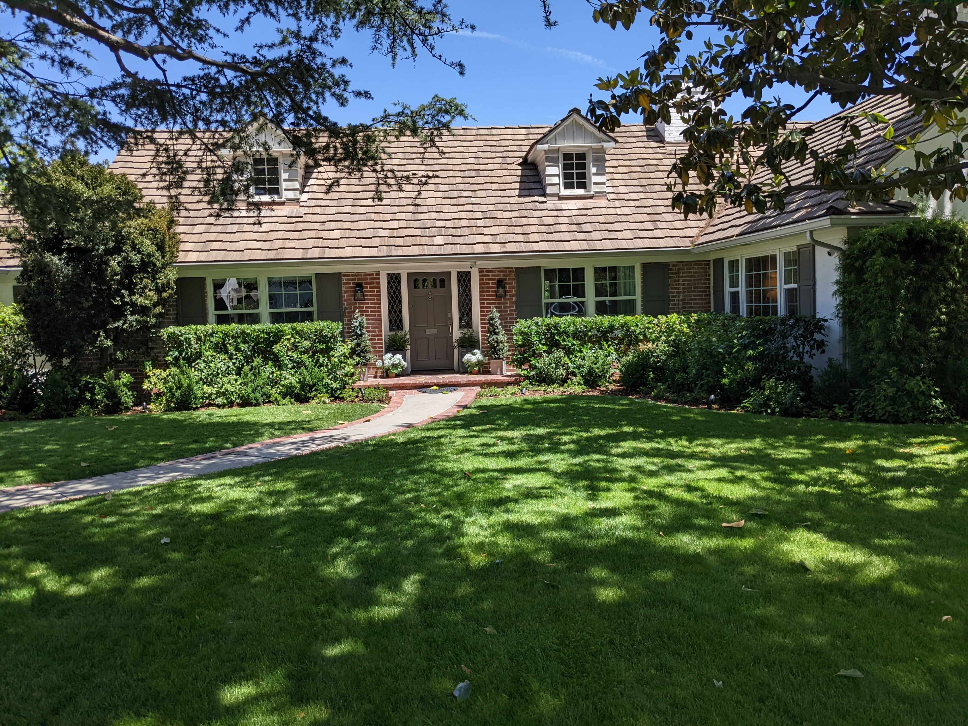 A single-story house with a sloped roof, set in a well-maintained yard featuring green grass and a pathway leading to the front door.