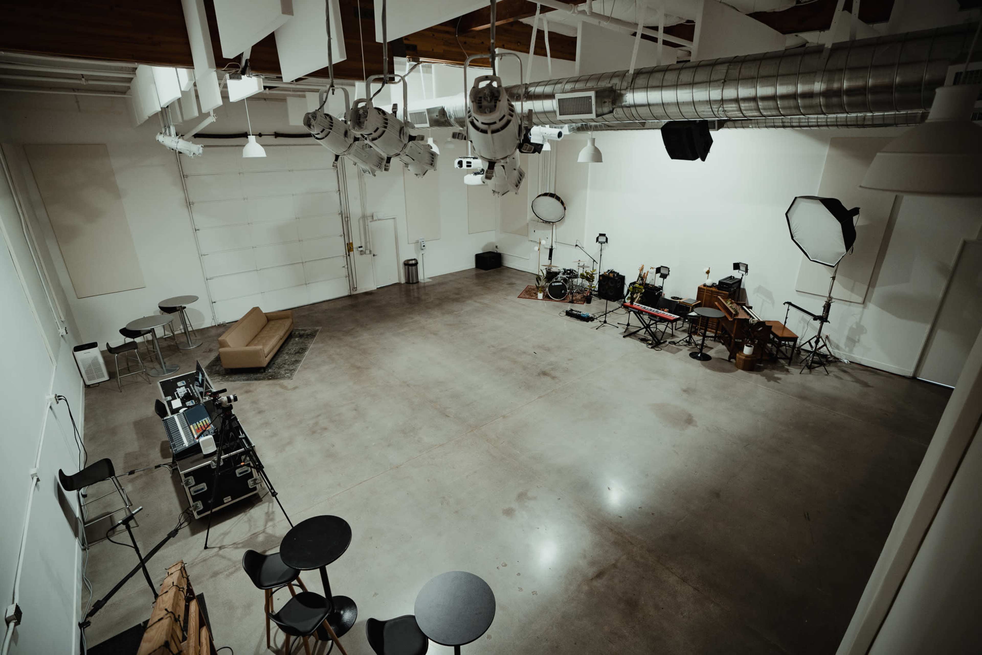 A spacious, empty studio with a concrete floor, various music and lighting equipment, and seating arranged around the perimeter.