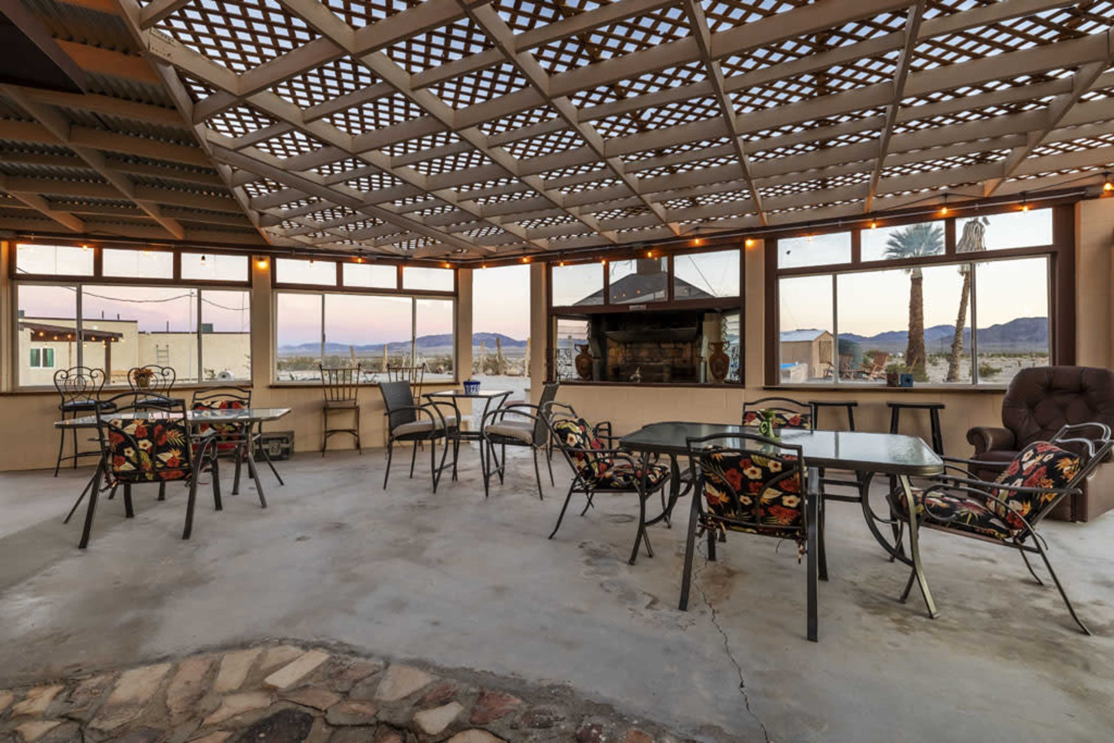 A spacious patio with metal furniture, a stone floor, and large windows overlooking a mountainous landscape.