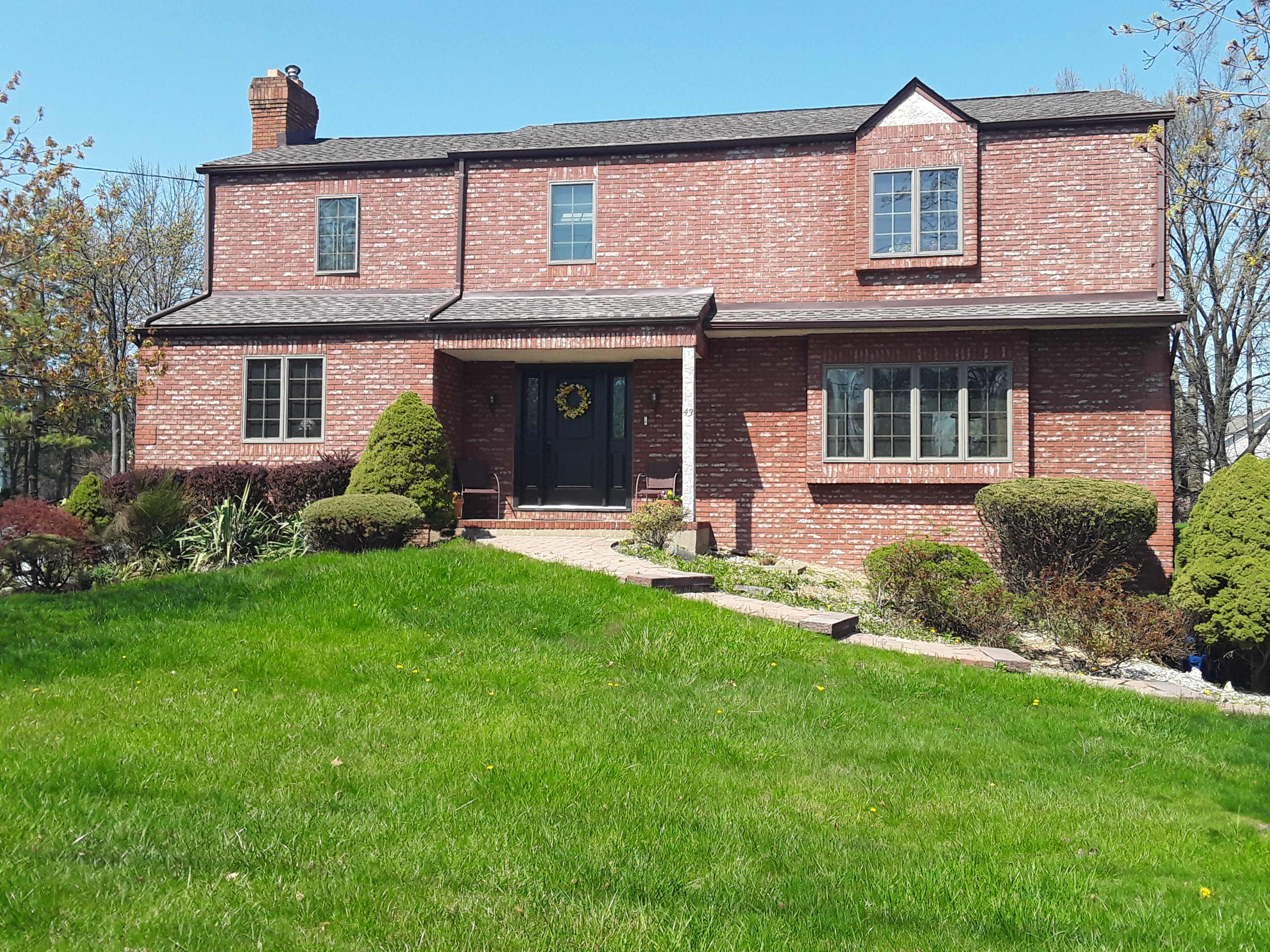 A two-story brick house with a landscaped front yard and a pathway leading to the entrance.