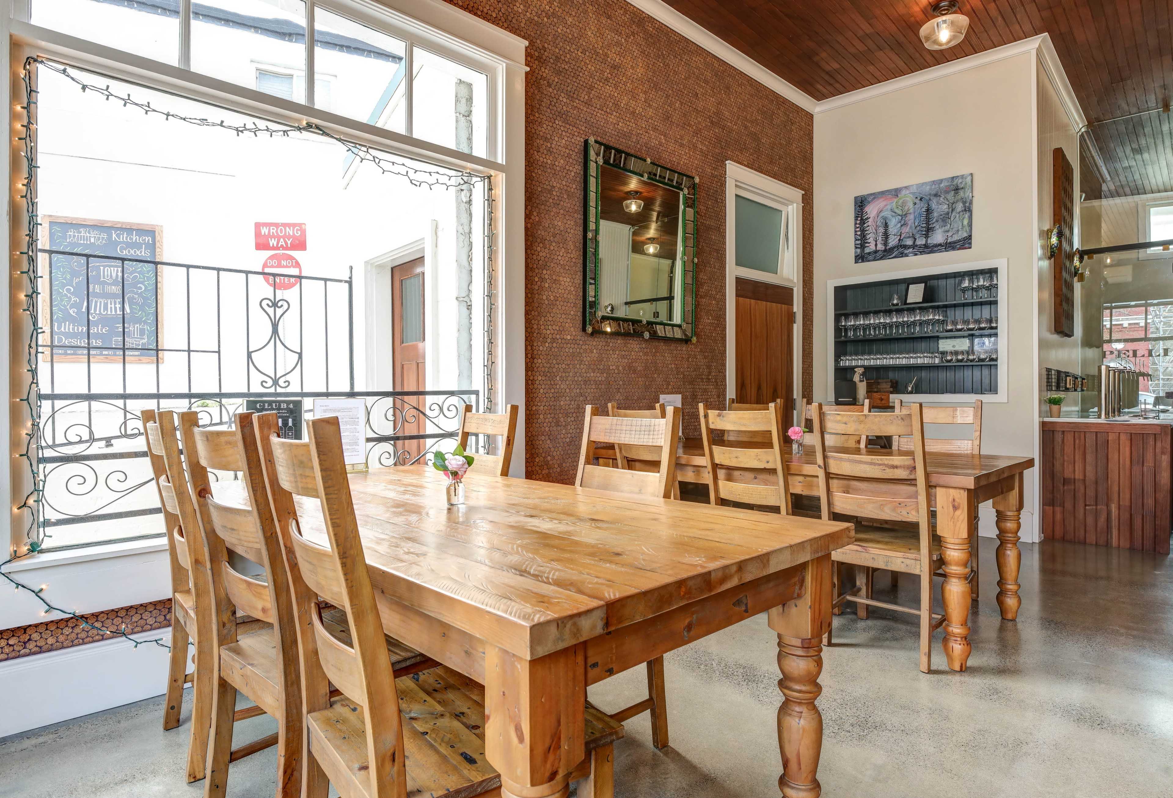 The image shows a wooden dining area with several tables and chairs, framed by a large window and a decorative mirror on the wall.