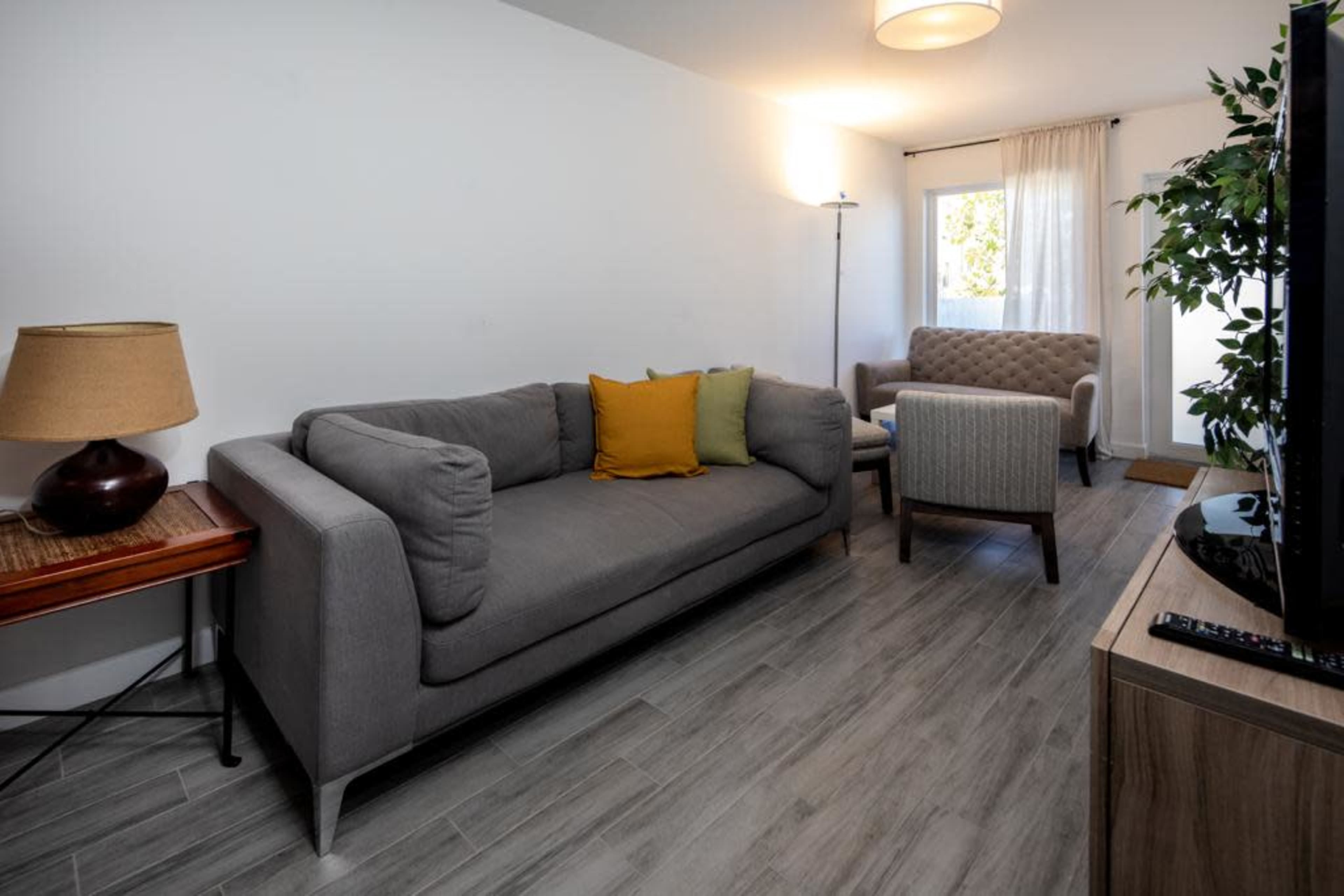 A modern living room with a gray sofa, a small armchair, a lamp, and a wooden side table.