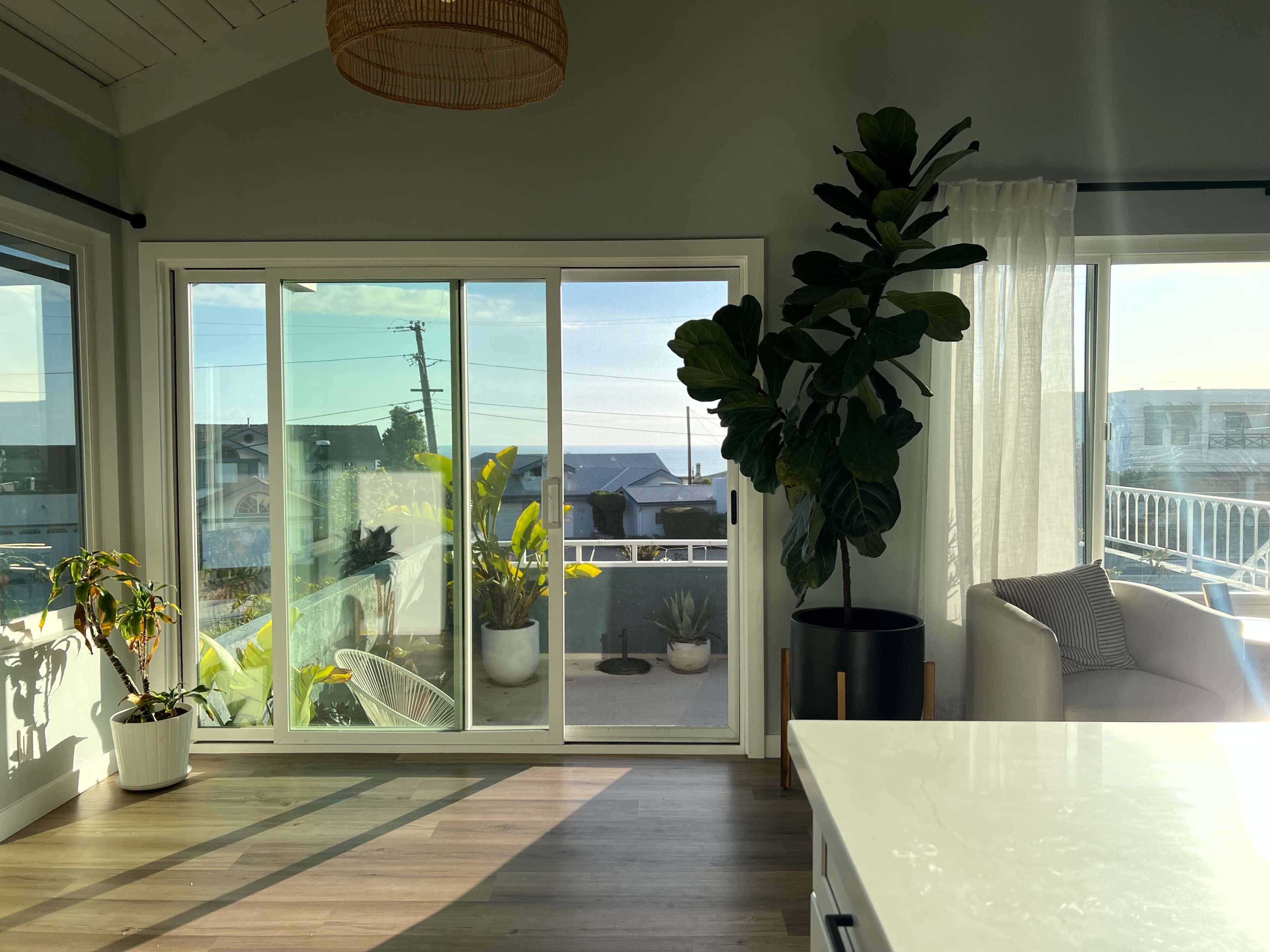 A brightly lit interior room with large sliding glass doors, a potted plant, and a cozy seating area near a kitchen countertop.