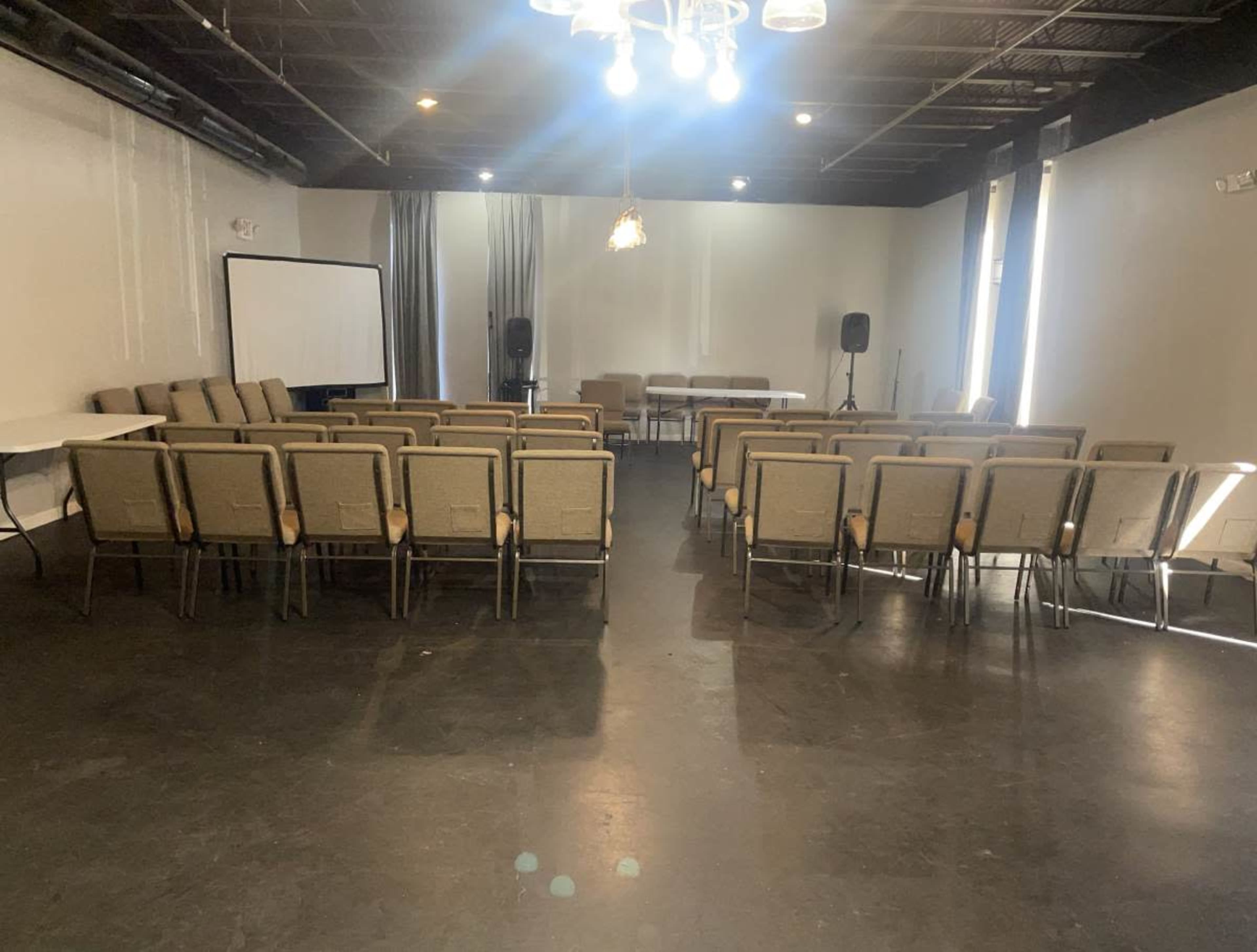 The image shows a conference room set up with several rows of chairs facing a central table and presentation screen.