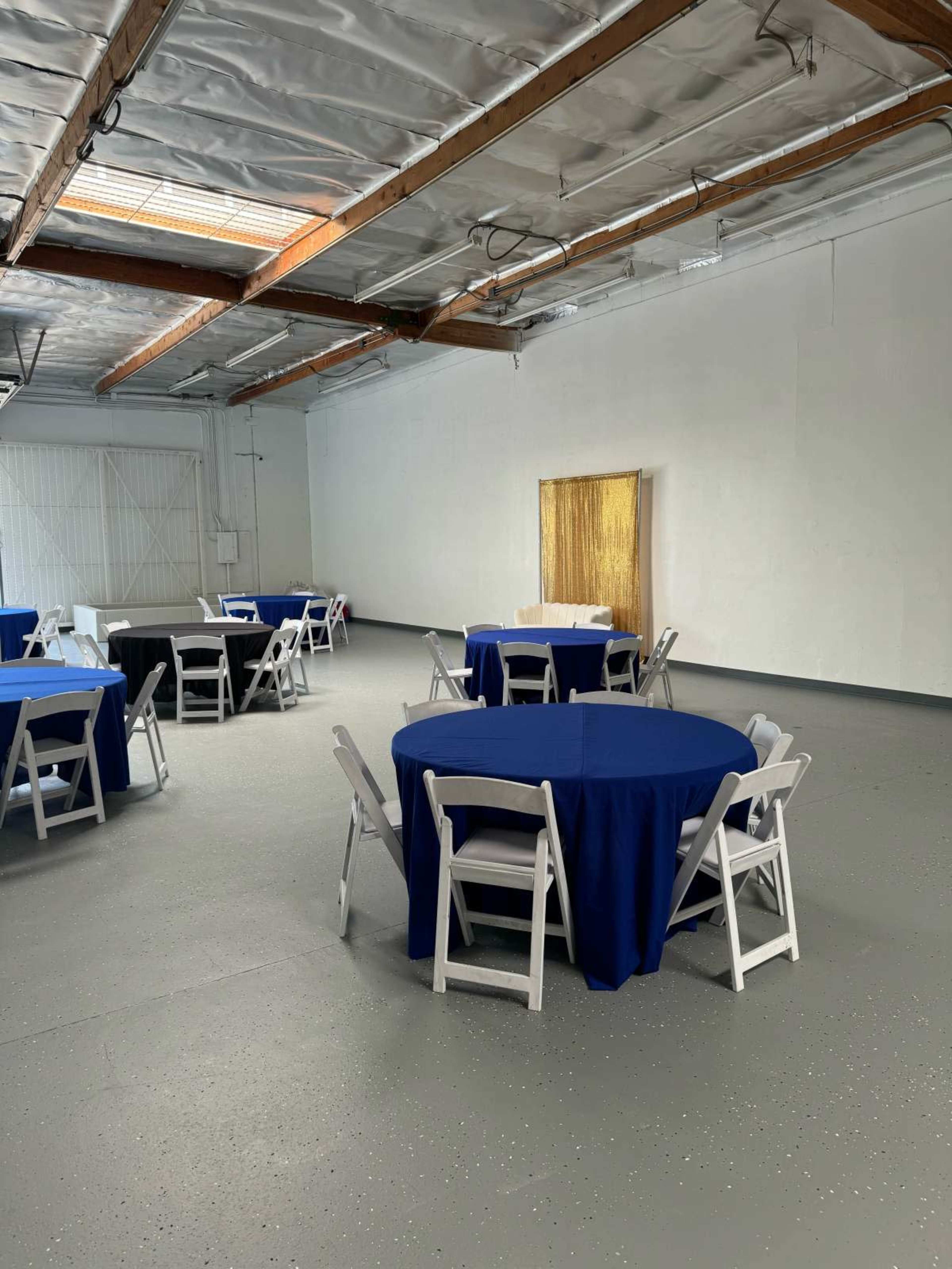 A spacious room with several round tables covered in blue tablecloths and white chairs arranged around them.