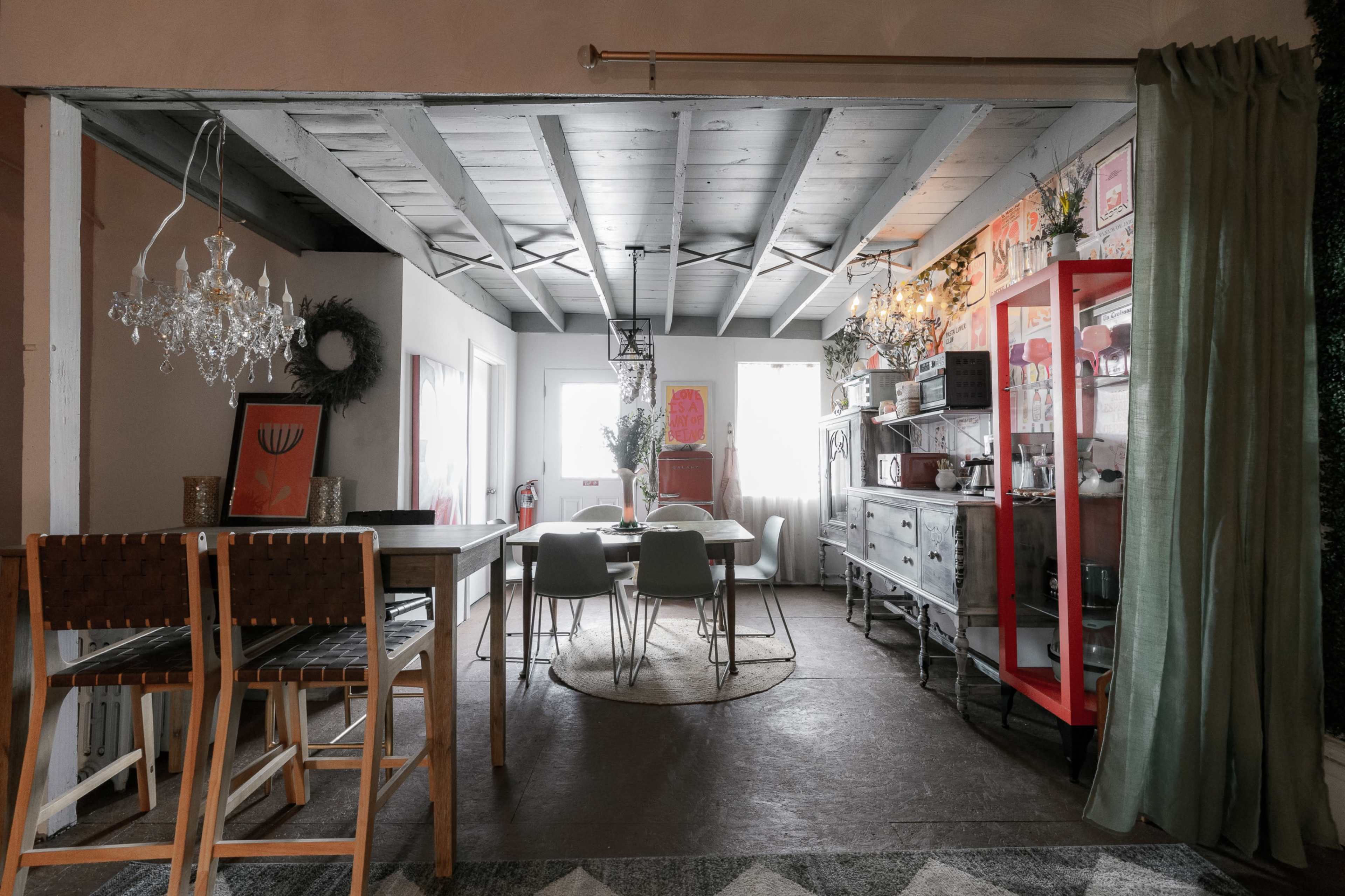 A spacious dining area with wooden beams, a large table, modern chairs, and decorative elements like a chandelier and a red cabinet.