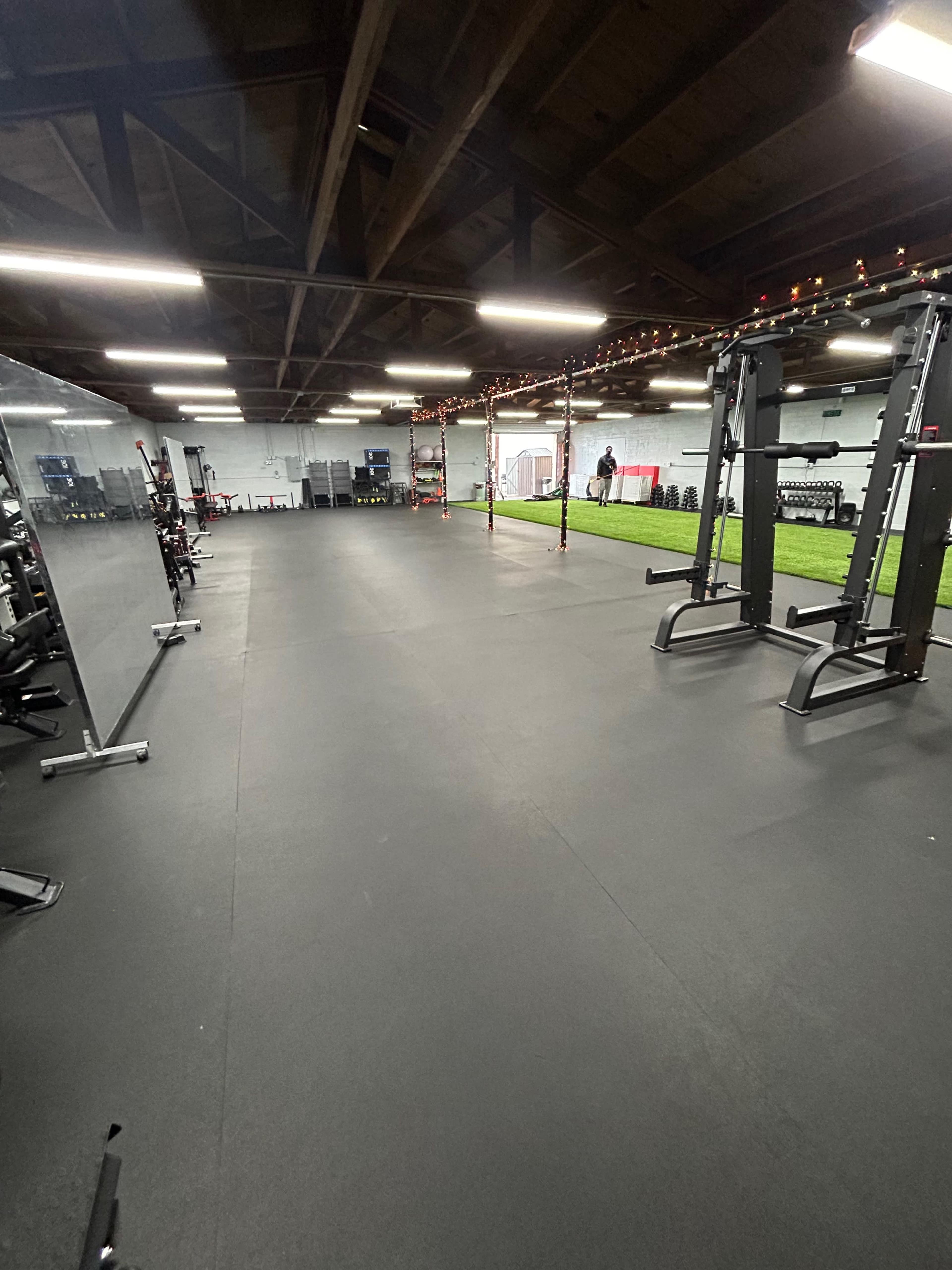 An empty gym space featuring weightlifting equipment, exercise mats, and artificial turf under a wooden ceiling.