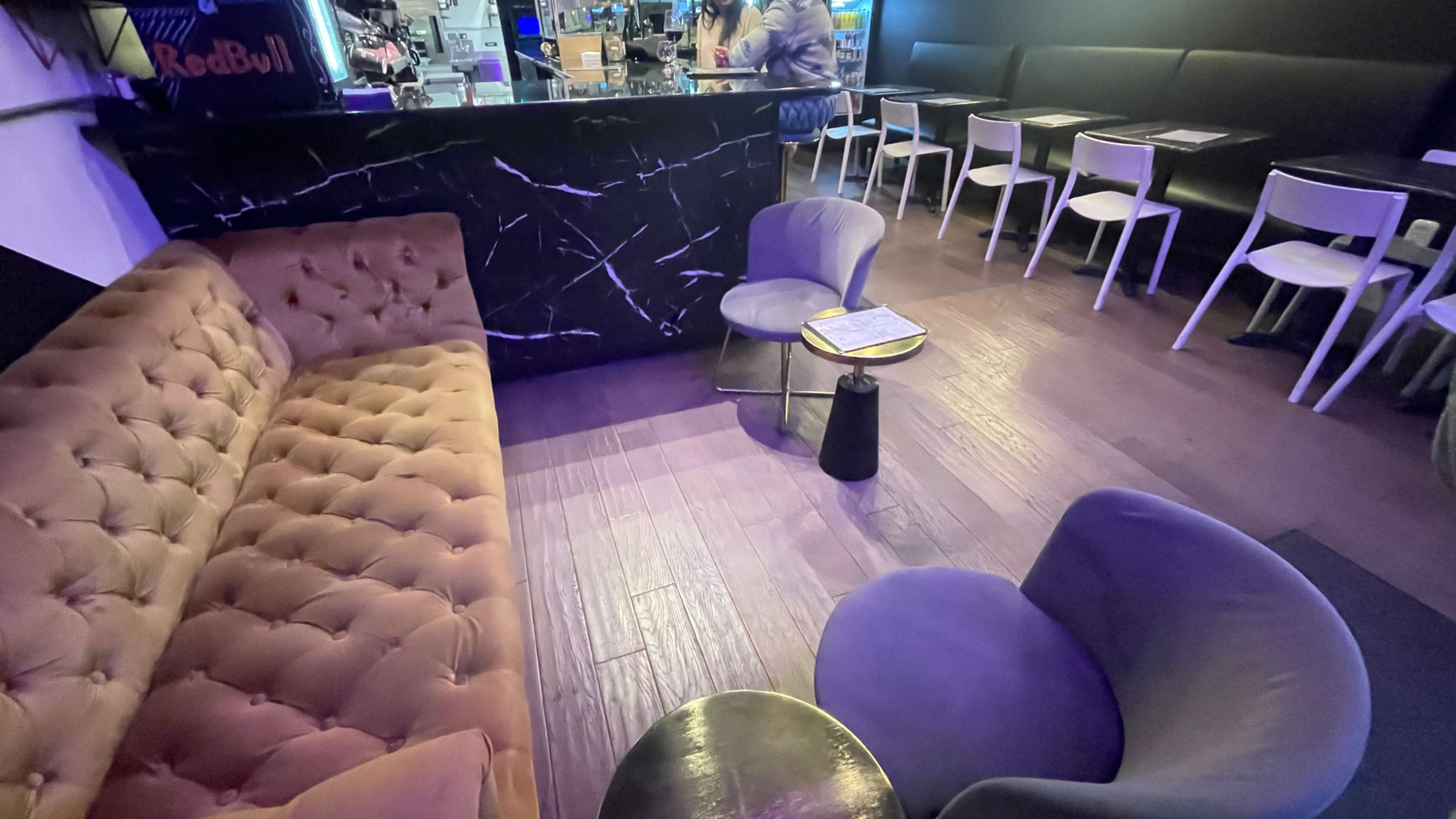 A cozy seating area in a lounge with a brown velvet sofa, two modern round chairs, and a small coffee table, all set against a dark bar backdrop.