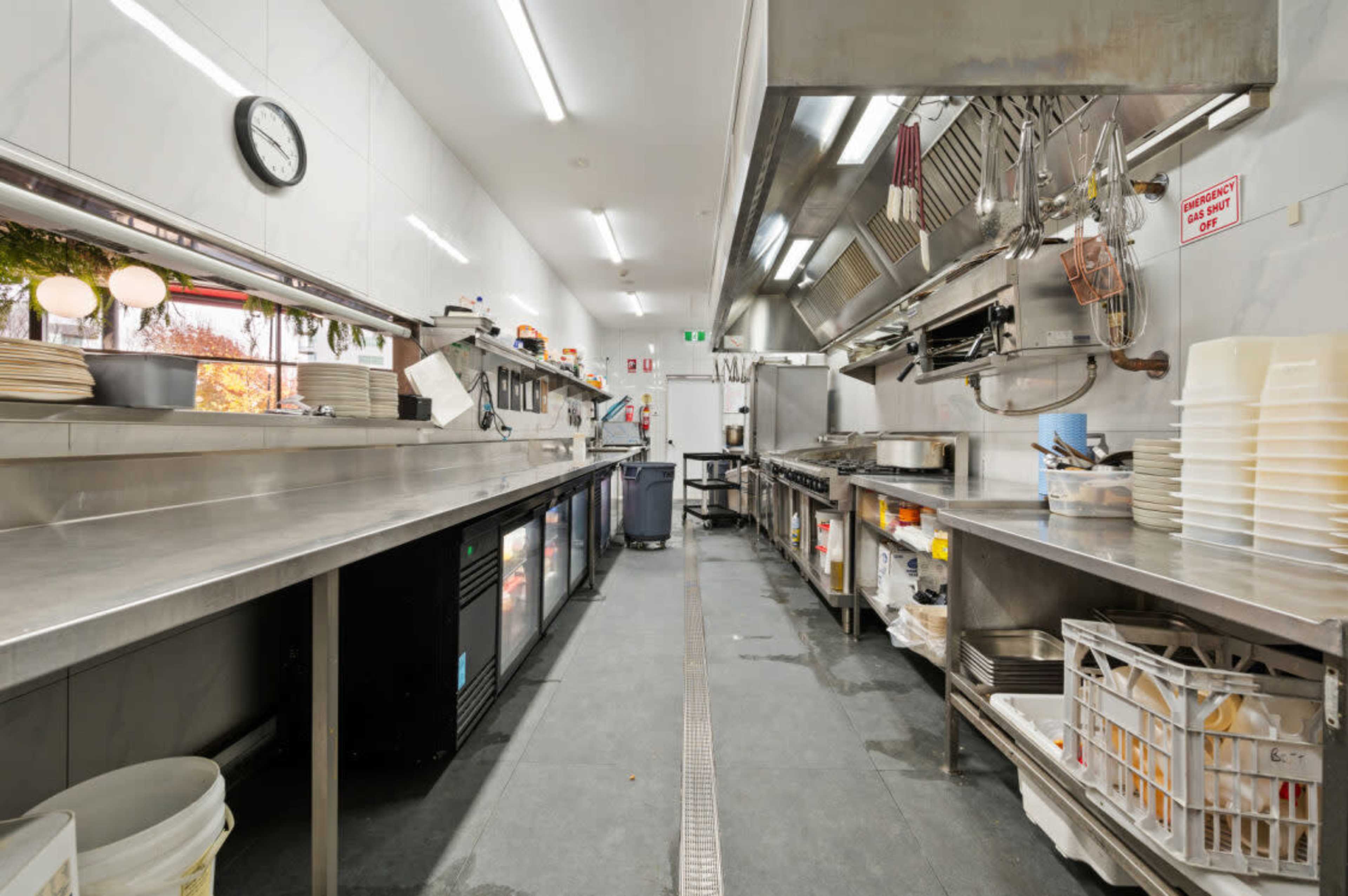 The image shows a commercial kitchen with stainless steel countertops, cooking equipment, and organized storage areas for utensils and ingredients.