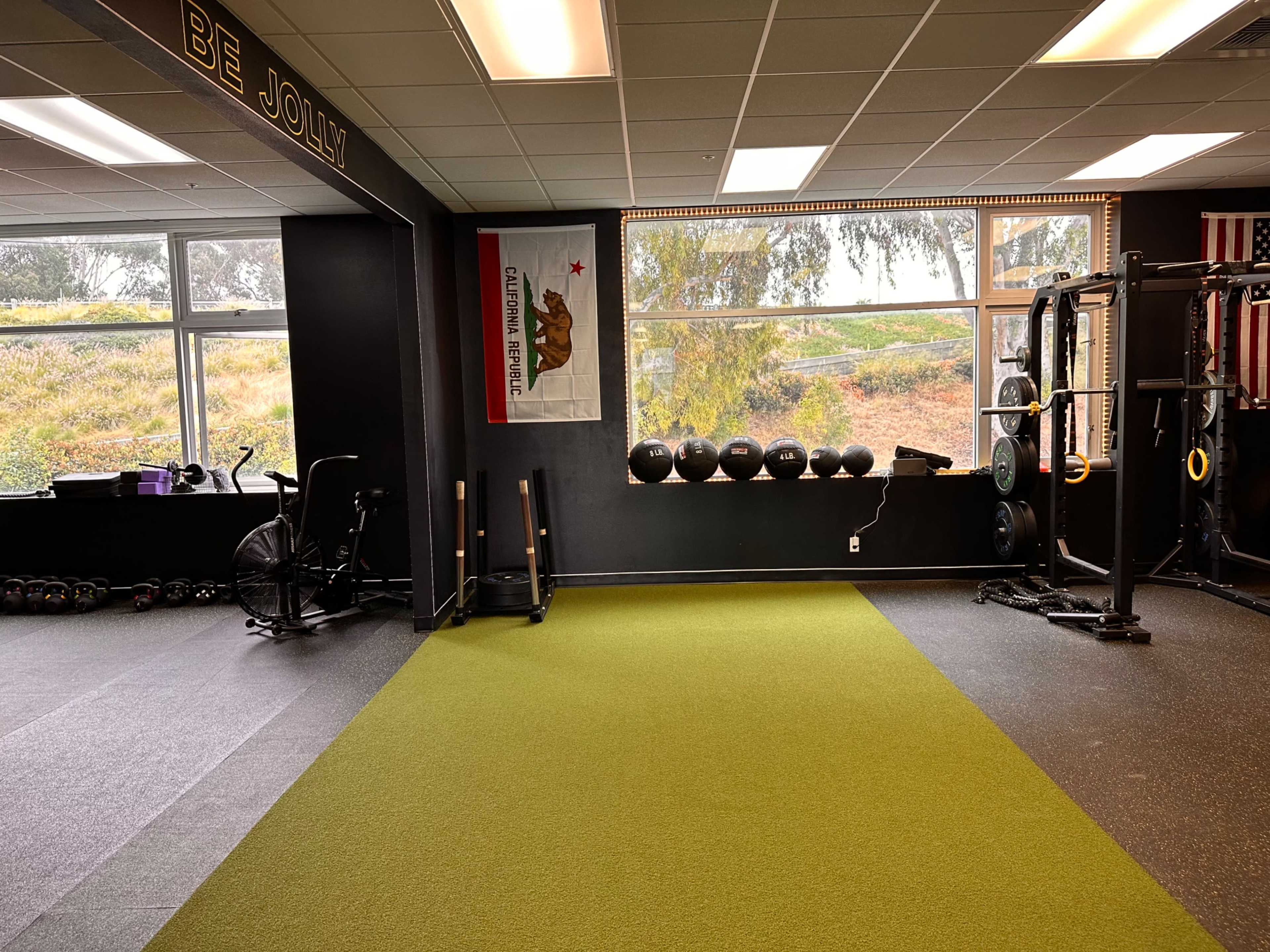 A fitness room featuring green turf, exercise equipment, and large windows with a view of the outdoors.
