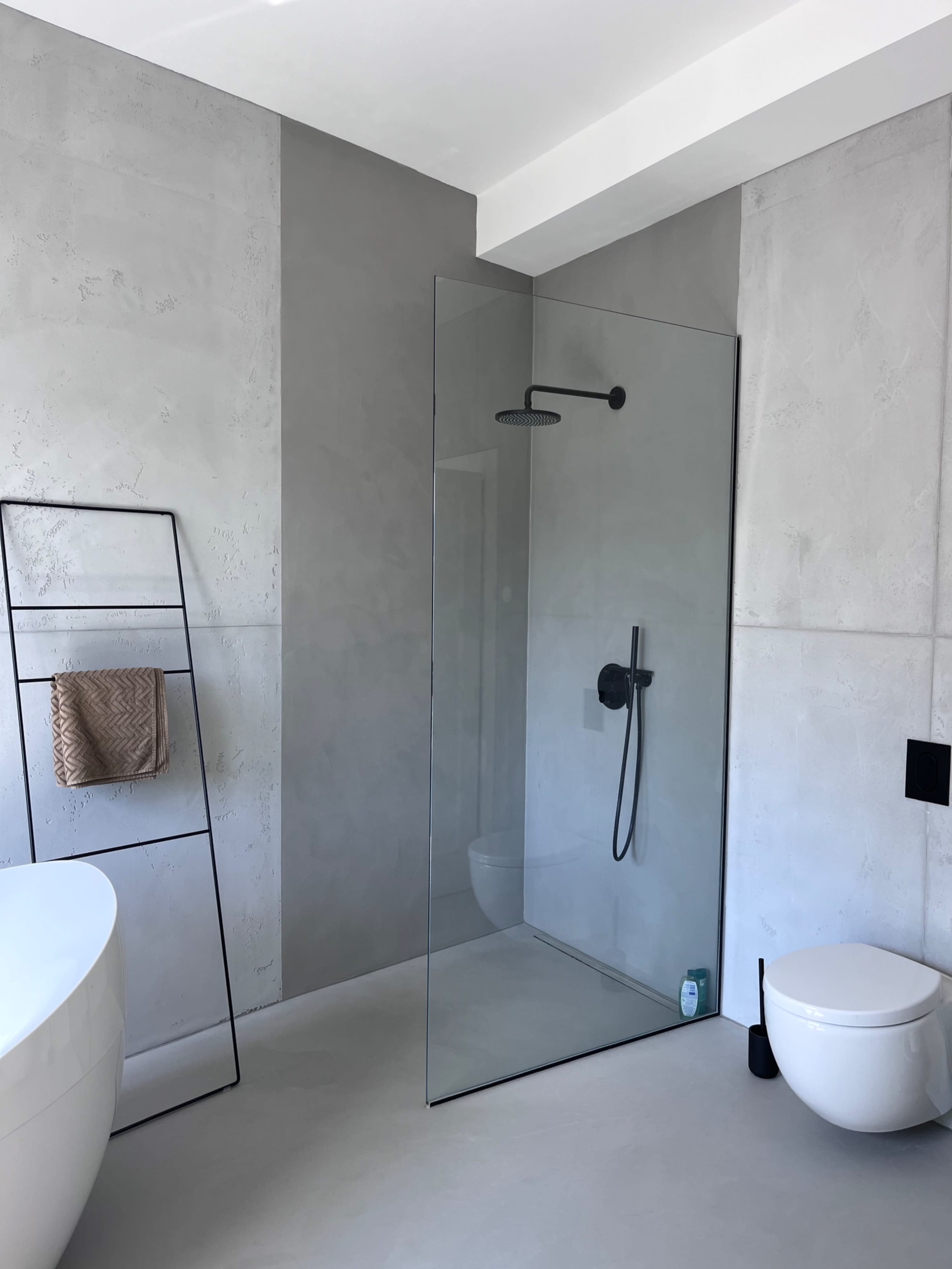 The image shows a modern bathroom featuring a glass shower, a freestanding bathtub, a wall-mounted toilet, and a towel rack.