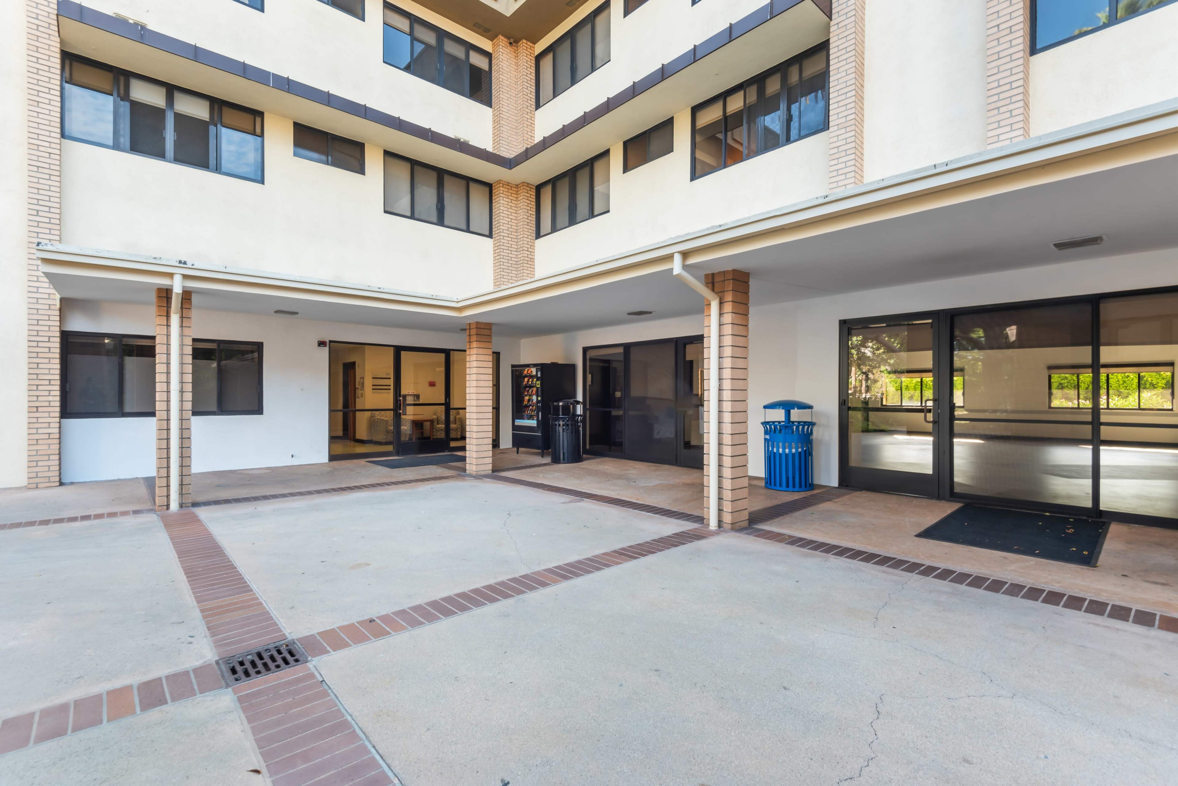 The image shows the entrance area of a multi-story building with large windows and a pavement courtyard.