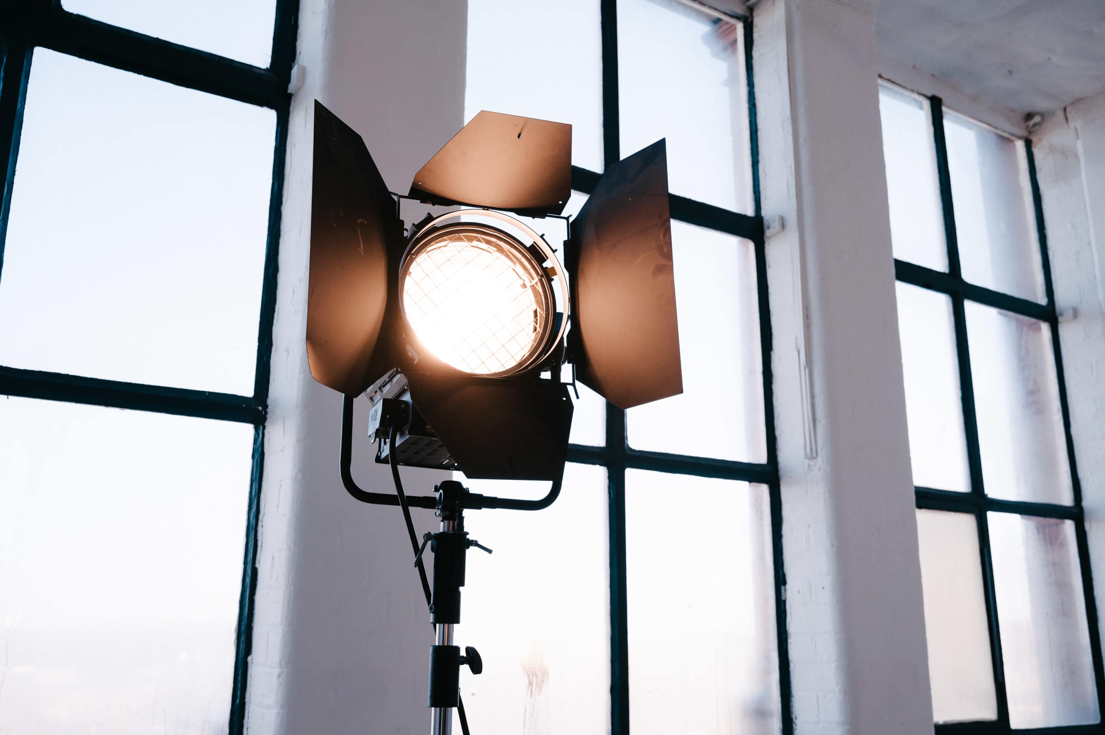 A studio spotlight is positioned in front of large windows in a well-lit space.
