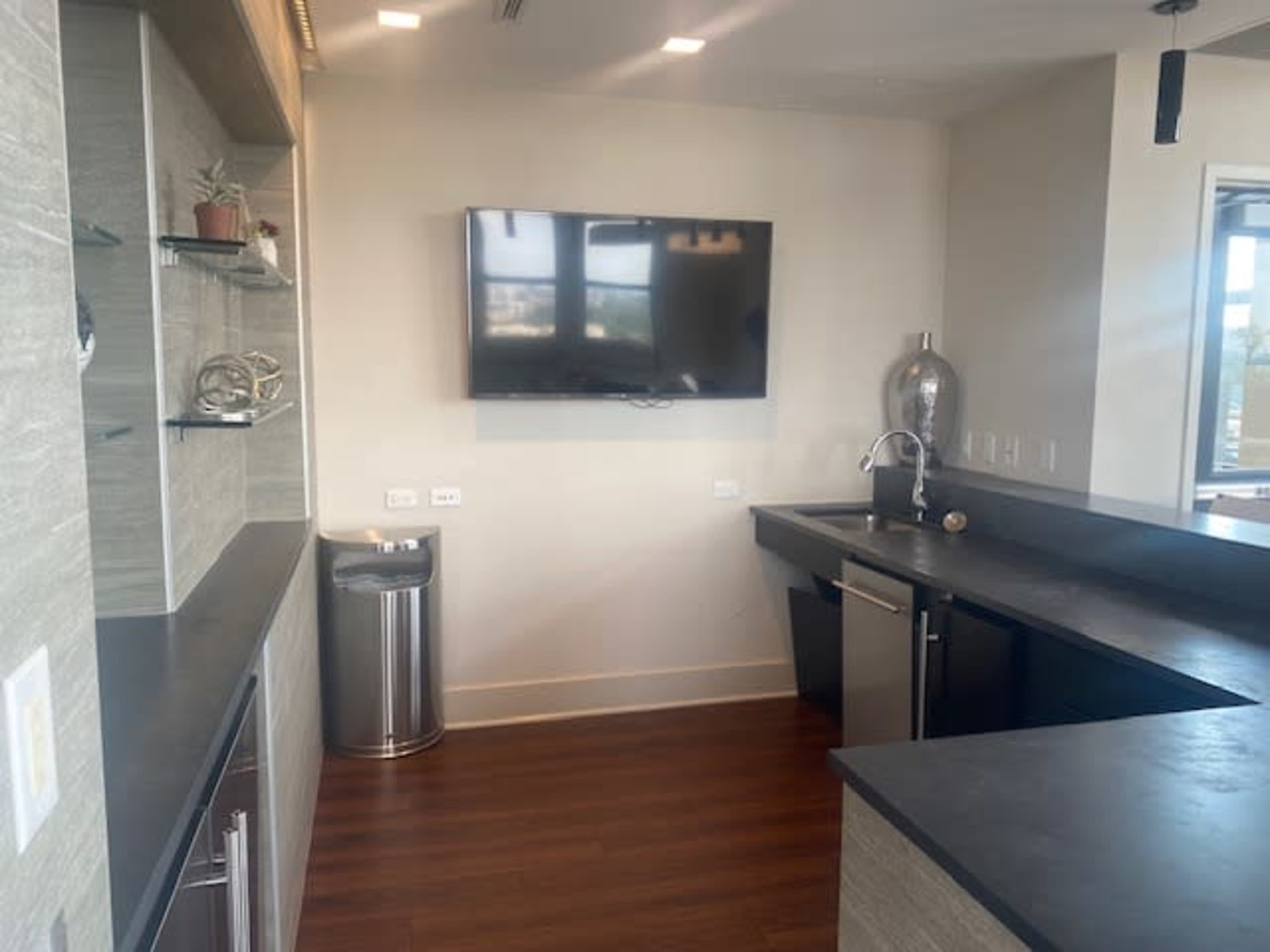 A modern kitchen area featuring a wall-mounted television, an angled countertop, and stainless steel appliances.